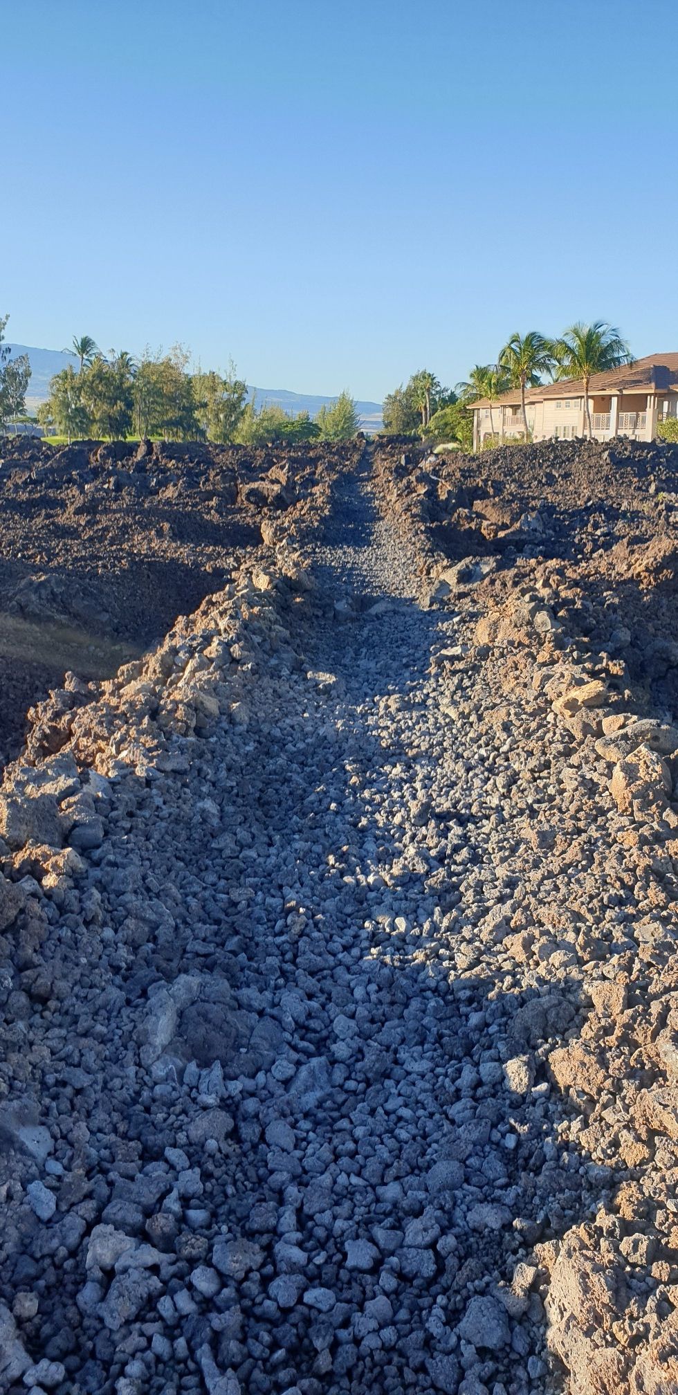 A narrow rocky path cuts through a field of dark, rough terrain. - Kiholo-Puako Trail