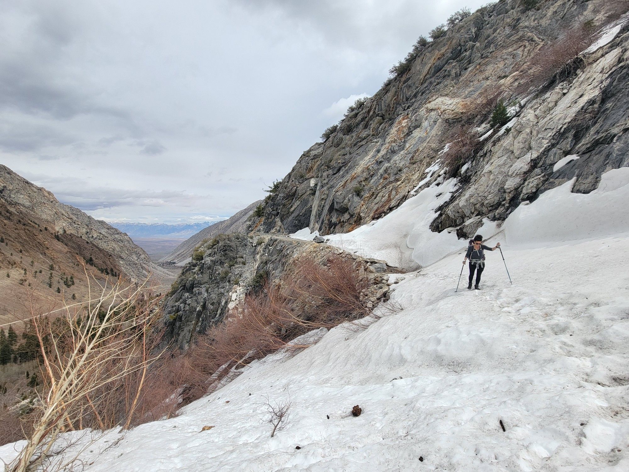 Hiker with poles on a snowy mountain path under an overcast sky. - Pine Creek Waterfall Overlook