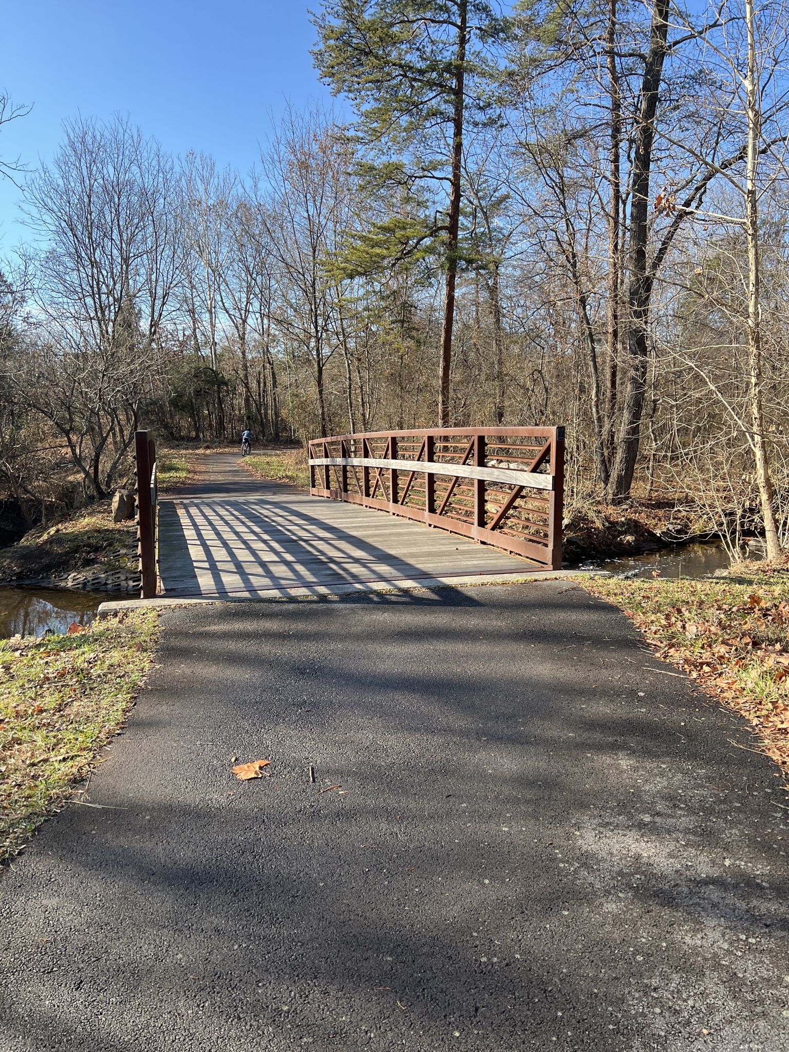 Paved path leading to a brown metal bridge over a stream on a sunny day. - Herndon Caboose Park – Green Lizard Cycling, Herndon loop from Herndon