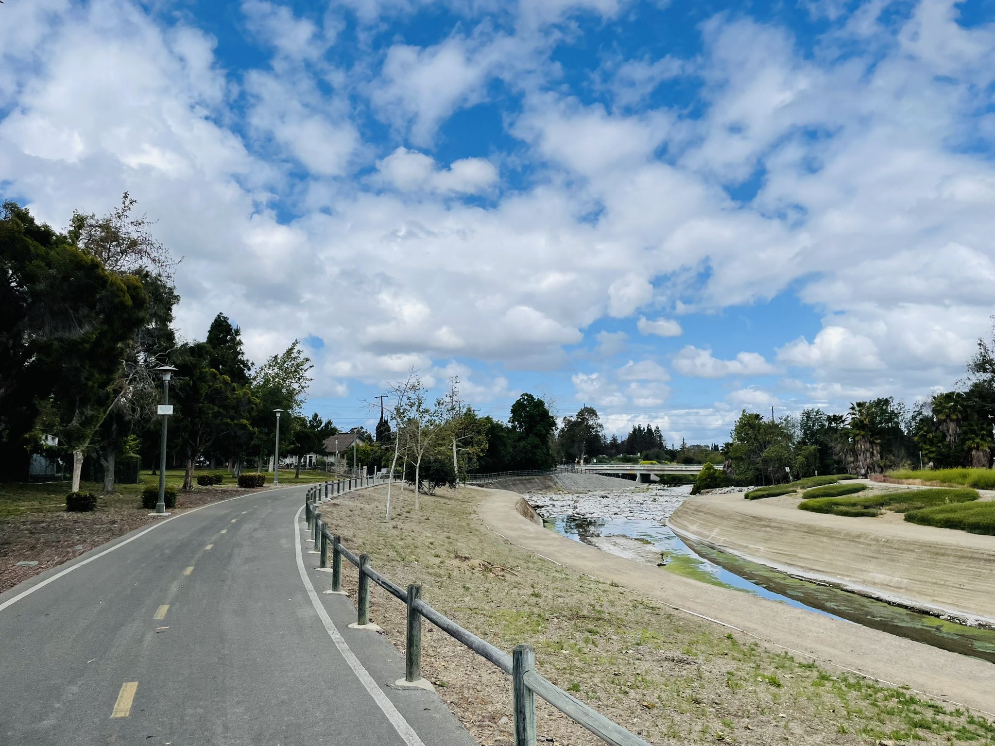 Paved path alongside a dry riverbed under a bright, cloudy sky. - Along Santiago Creek – Historic Dam loop from Santa Ana College