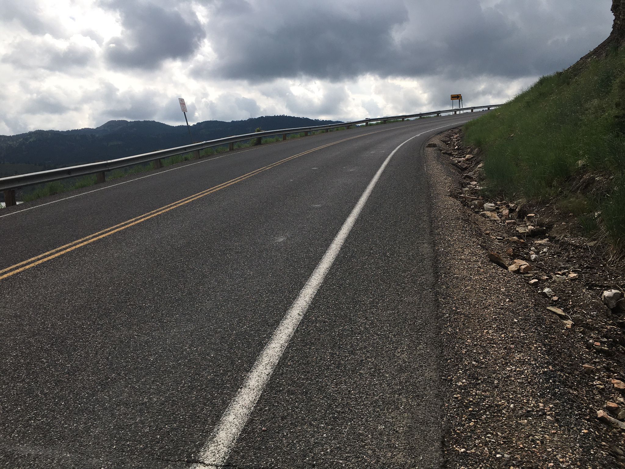 An empty paved road curves uphill with dark clouds overhead. - Bingham Hill and the Horsetooth Reservoir Dams loop