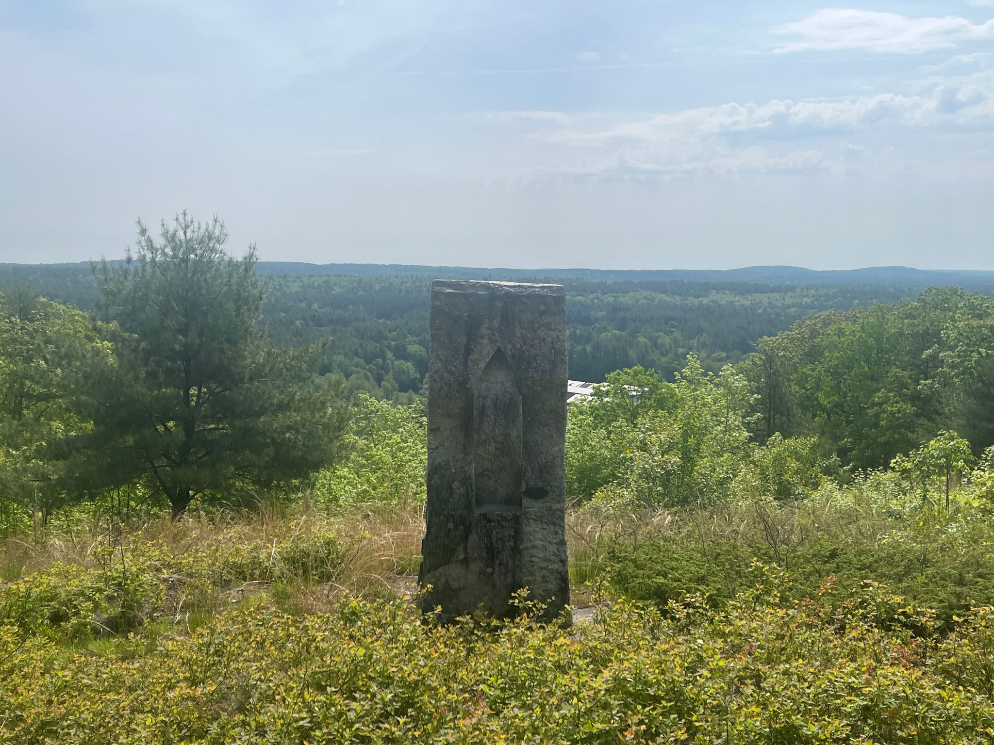 Dark stone monument overlooks a vast green forest under a bright sky. - Potanipo Hill Southway Trail Loop