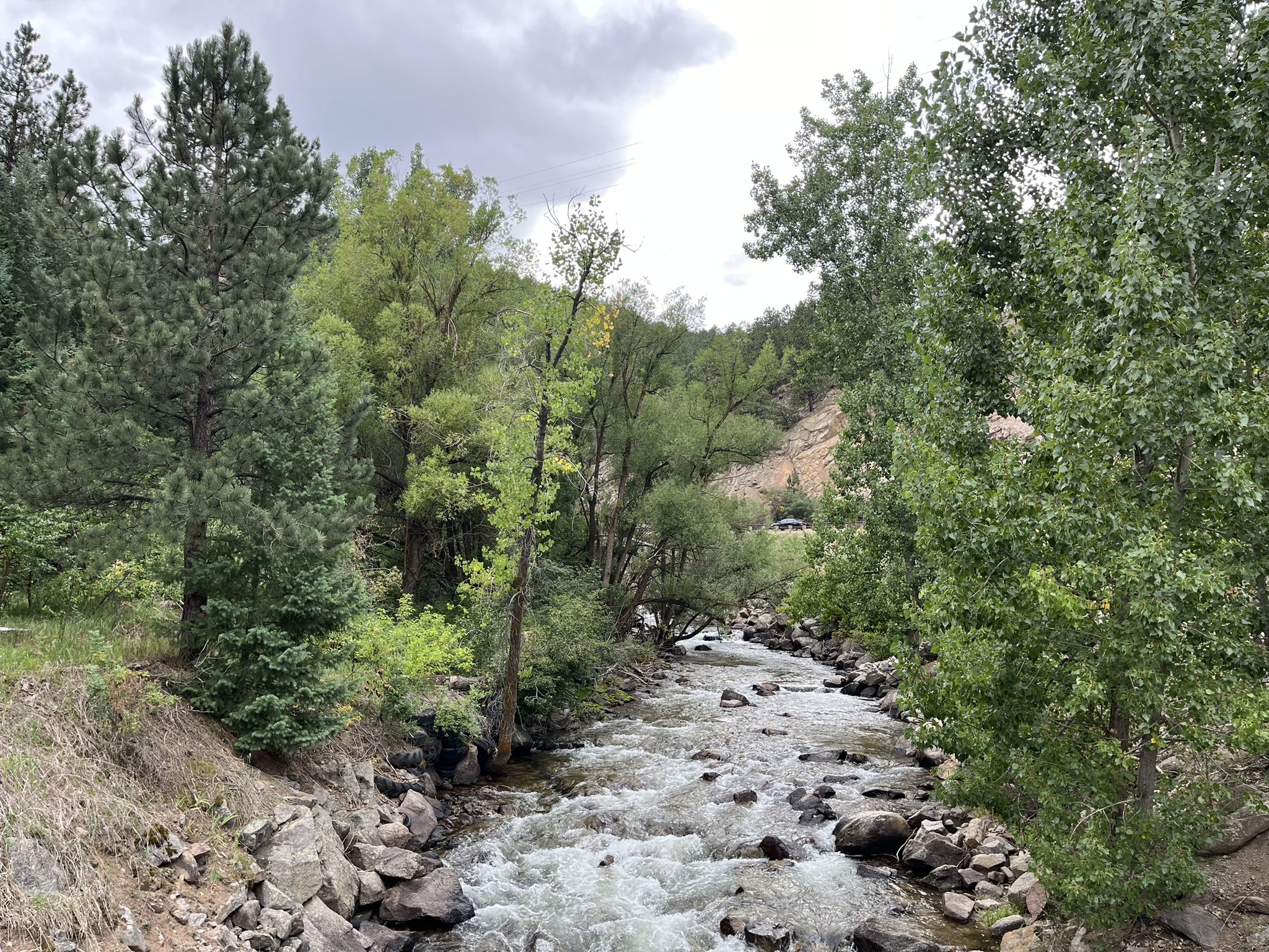 A rocky river flows through a lush, green valley under an overcast sky. - Gold Hill via Fourmile and Sunshine Canyons