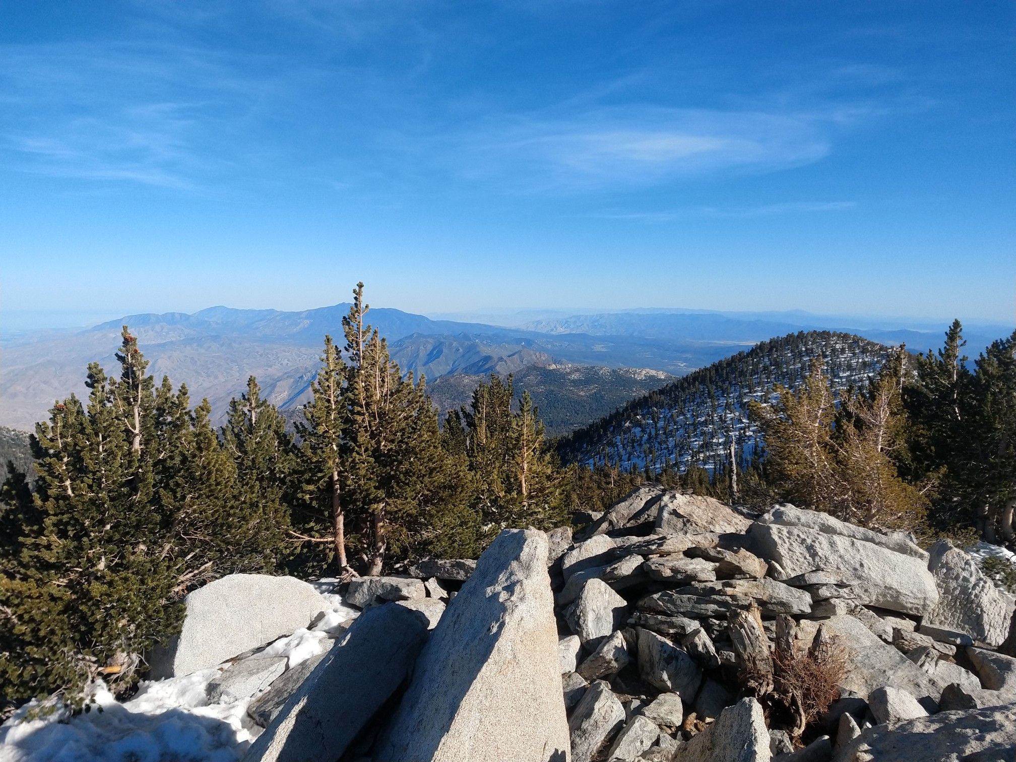 Rocky mountain peak with pine trees and snow, overlooking hazy distant mountains. - San Jacinto Peak via Deer Springs Trail