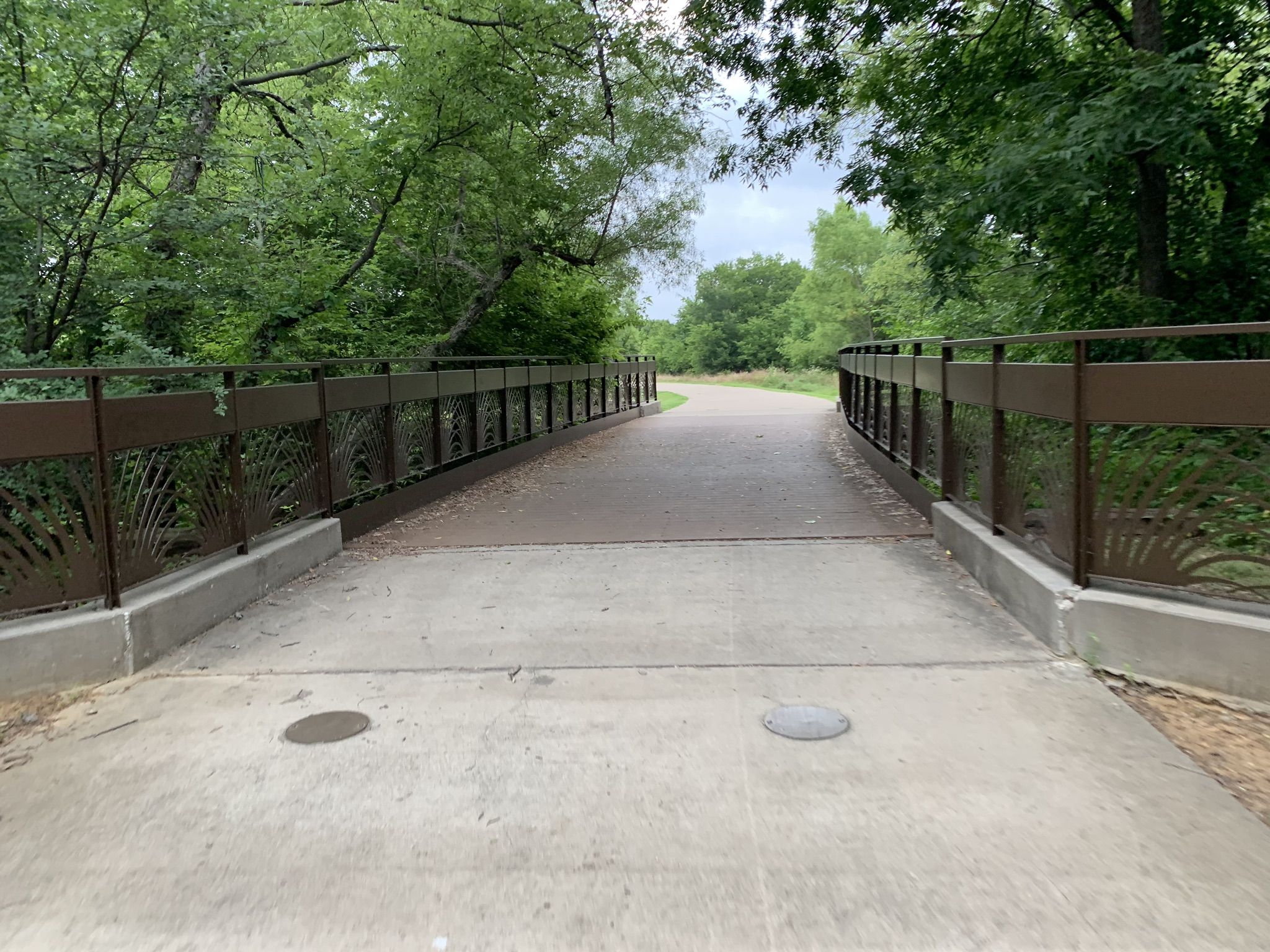 A concrete bridge with decorative railings surrounded by dense green trees. - DFW Discovery Trail: Mike Lewis Park Loop