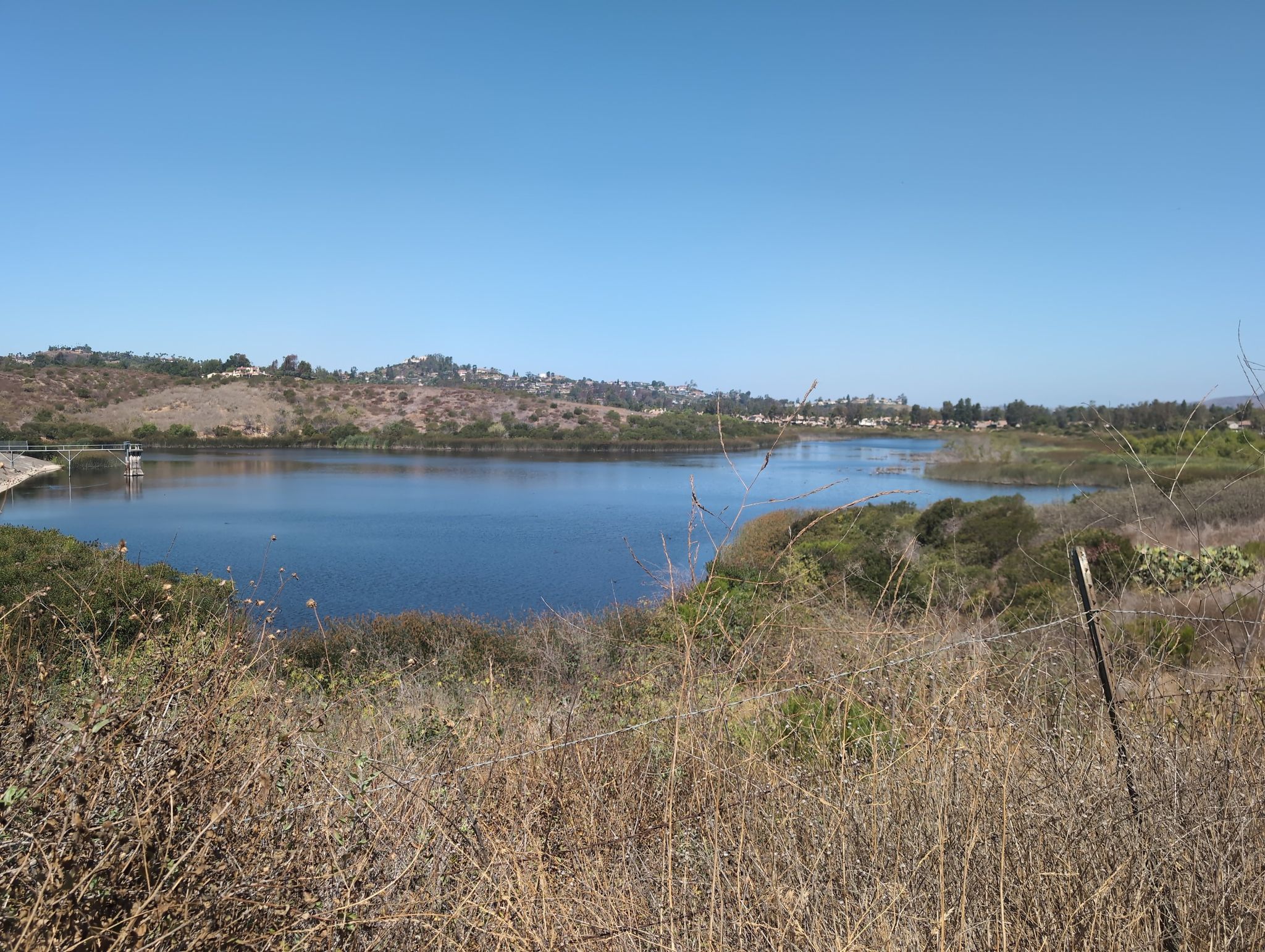 A wide blue lake surrounded by dry and green hills under a clear sky. - Santiago Canyon Road loop from Tustin