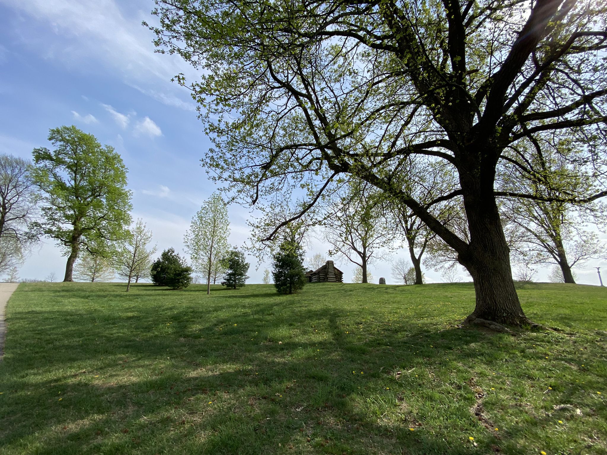 Grassy hill with large trees, distant stone building, bright sunny day. - Joseph Plumb Martin Trail Loop