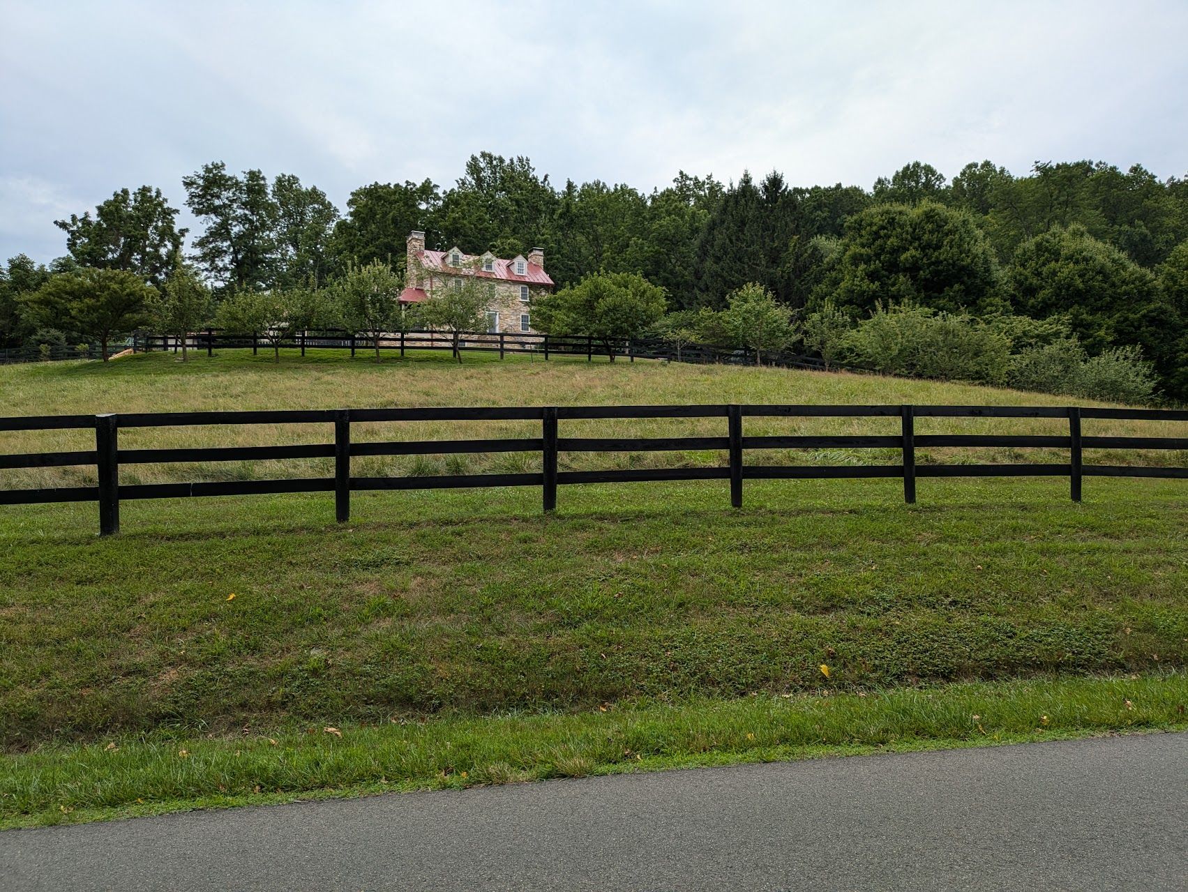 A black wooden fence crosses a green field with a distant building and trees. - Hopewell Gap loop from The Plains, Virginia