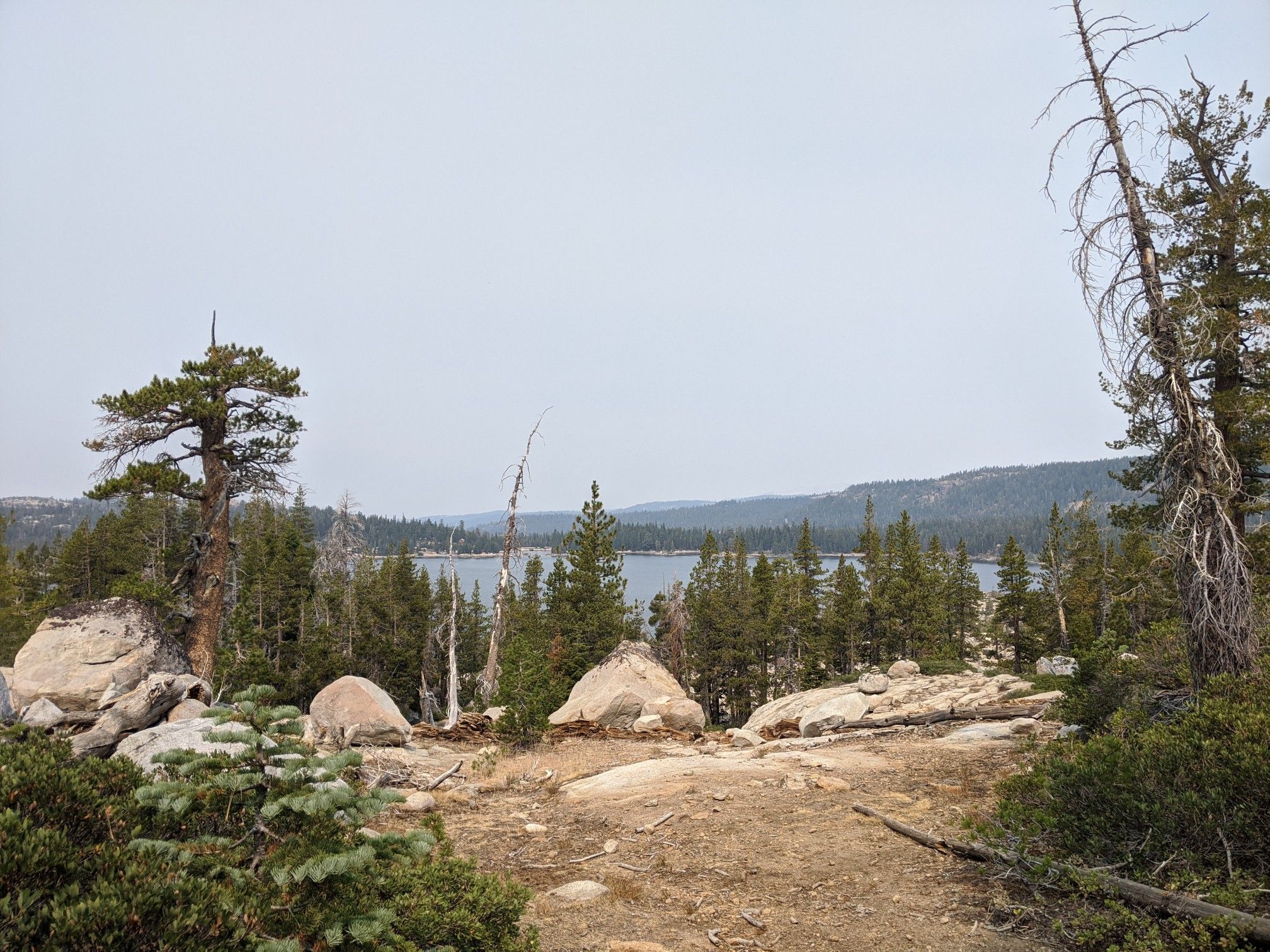 Overcast view of a lake surrounded by pine trees and large rocks. - Amy Lake and Granite Lake Trail