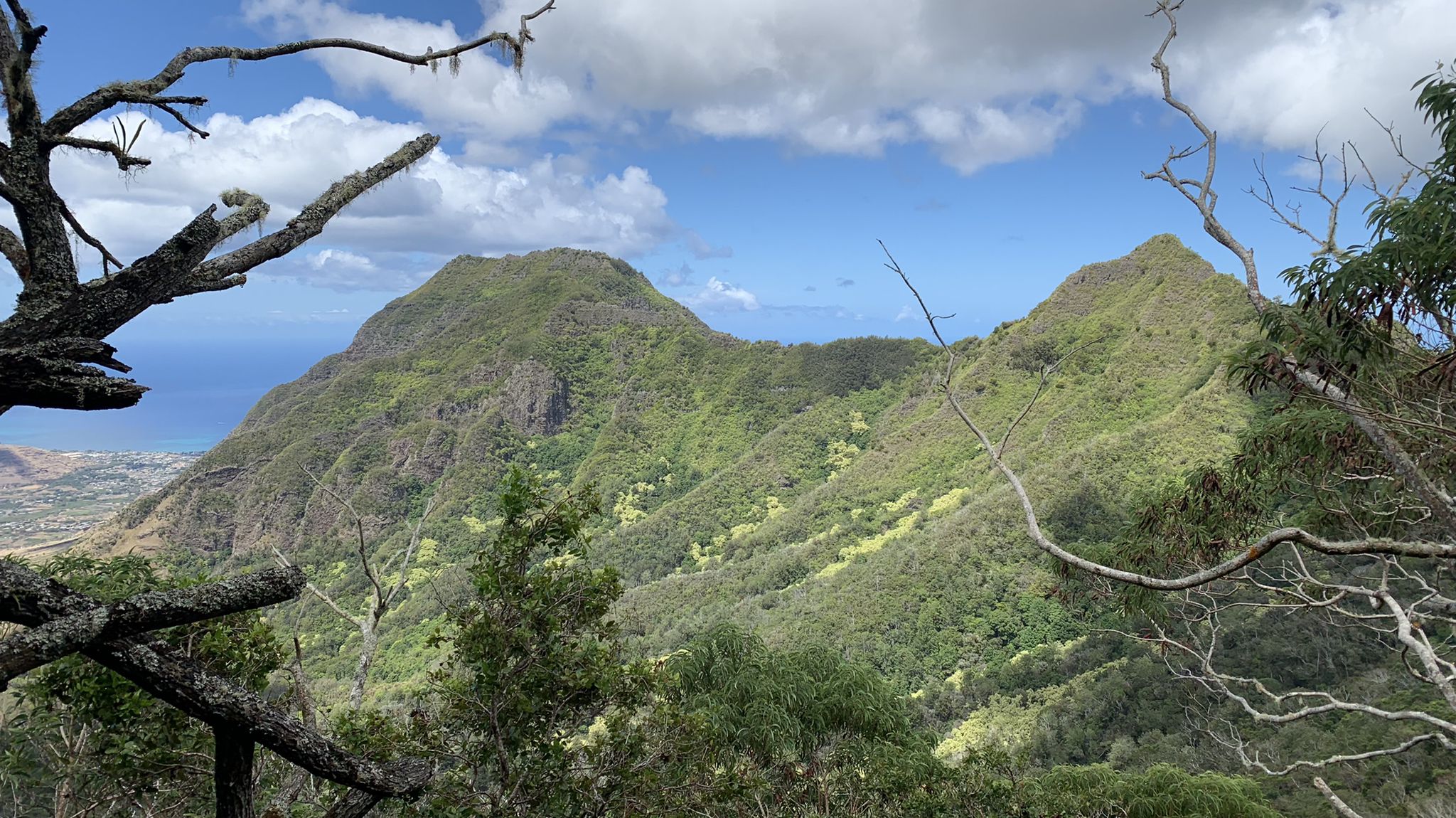 Lush green mountains under a partly cloudy sky, with distant ocean. - Mount Ka'ala Trail