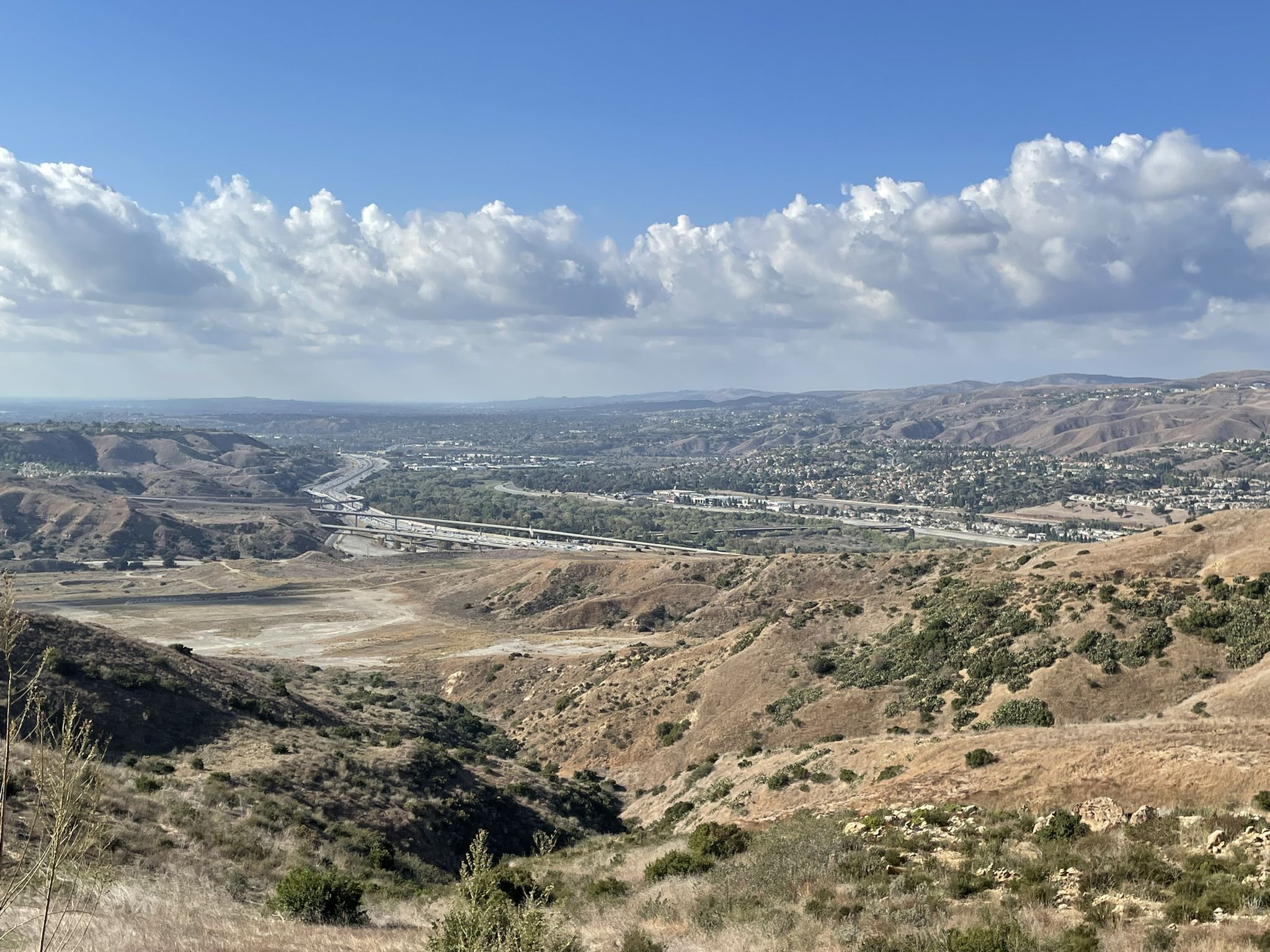 Sunny panoramic view of a dry valley with hills, highway, and distant town. - Sierra Peak via Coal Canyon Trail Loop