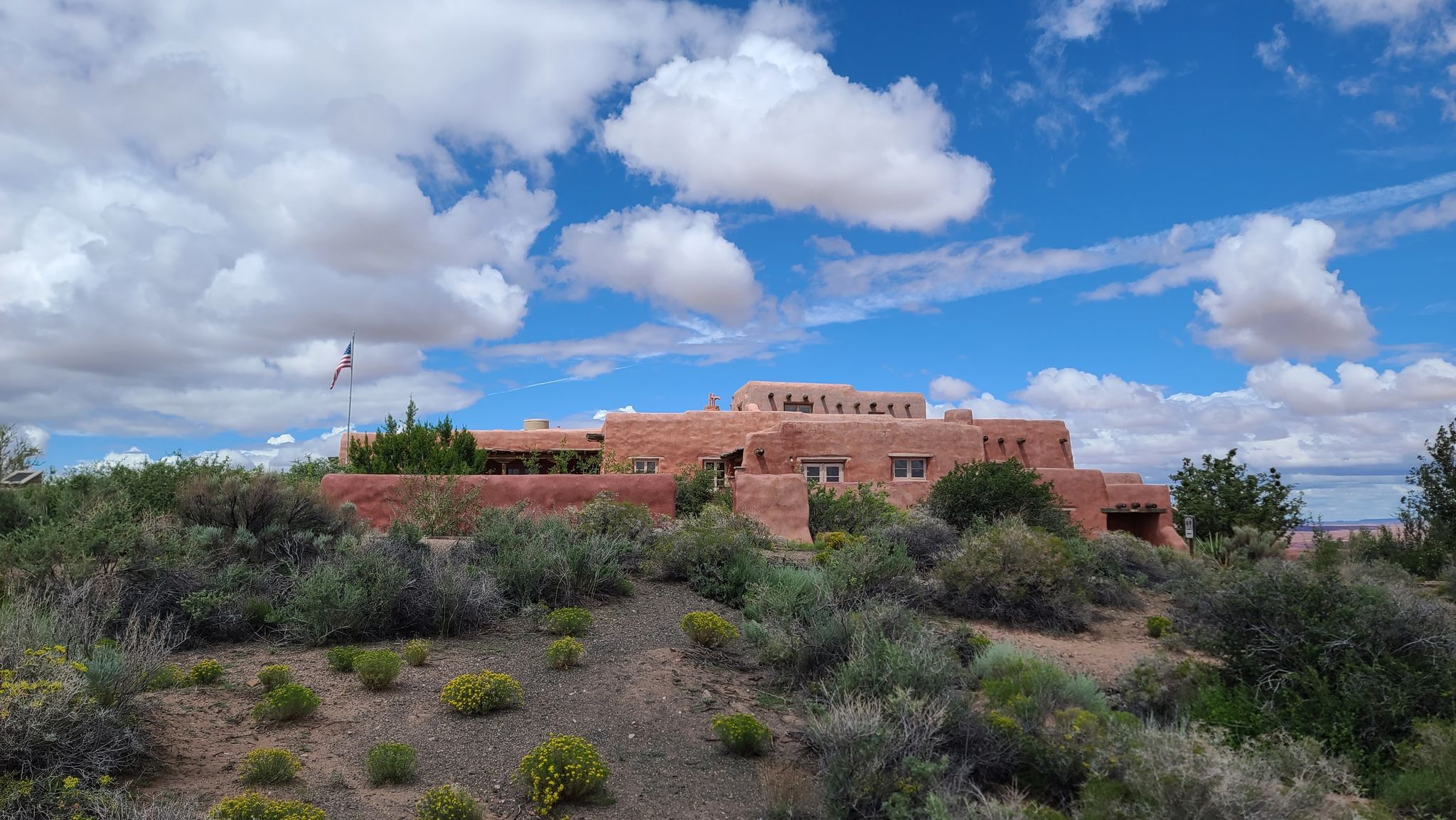 Red adobe building on a hill with green bushes under a cloudy sky. - Painted Desert Rim Trail