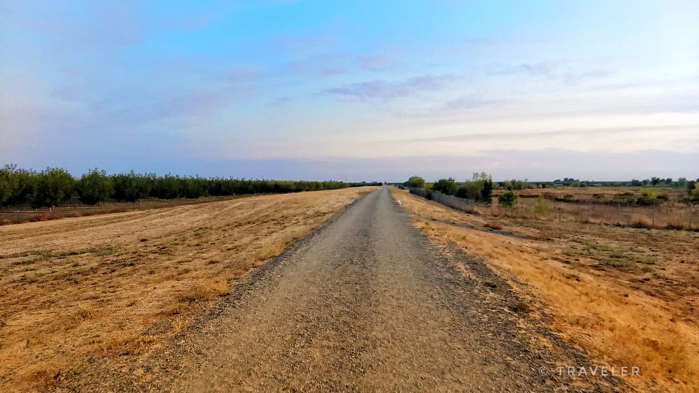 A long, straight dirt road extends through dry fields under a blue sky. - Valley Glen Drainage Pond