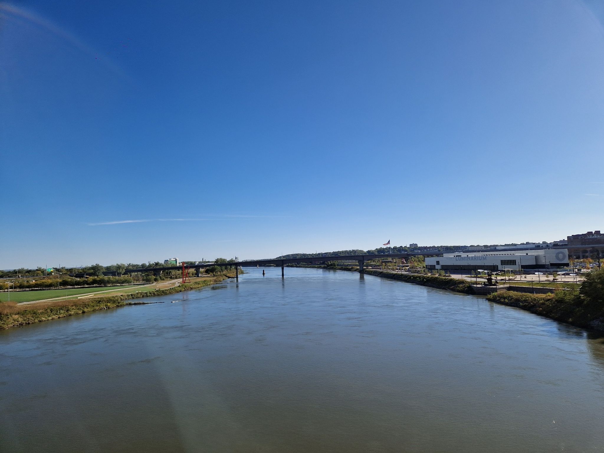 Wide river under a clear blue sky, with a distant bridge and buildings. - Bob Kerrey Pedestrian Bridge Trail