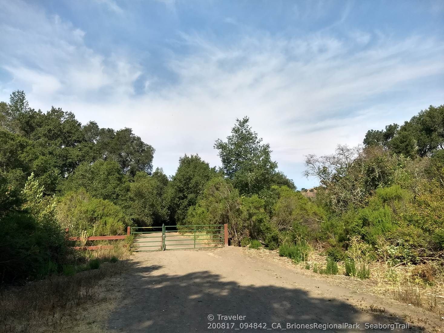 Dirt road leading to a metal gate, surrounded by dense green trees. - Seaborg and Crescent Ridge Trail Loop