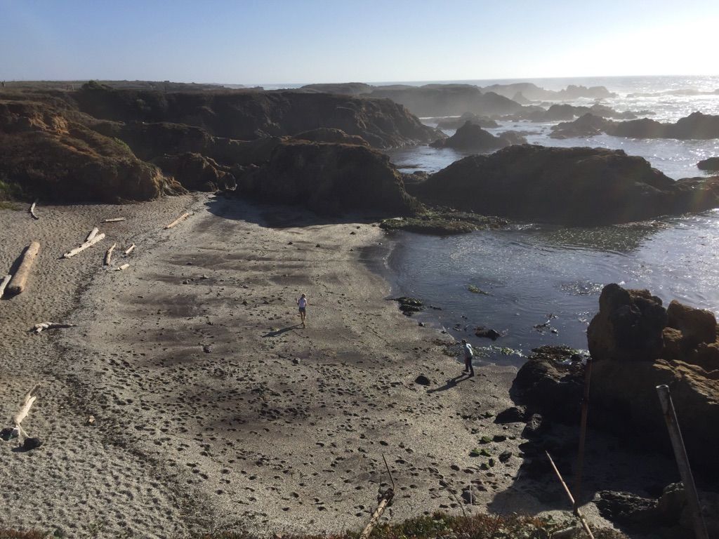Sunny beach with driftwood, rocky bluffs, and two people walking. - Noyo Headlands Park loop from Fort Bragg