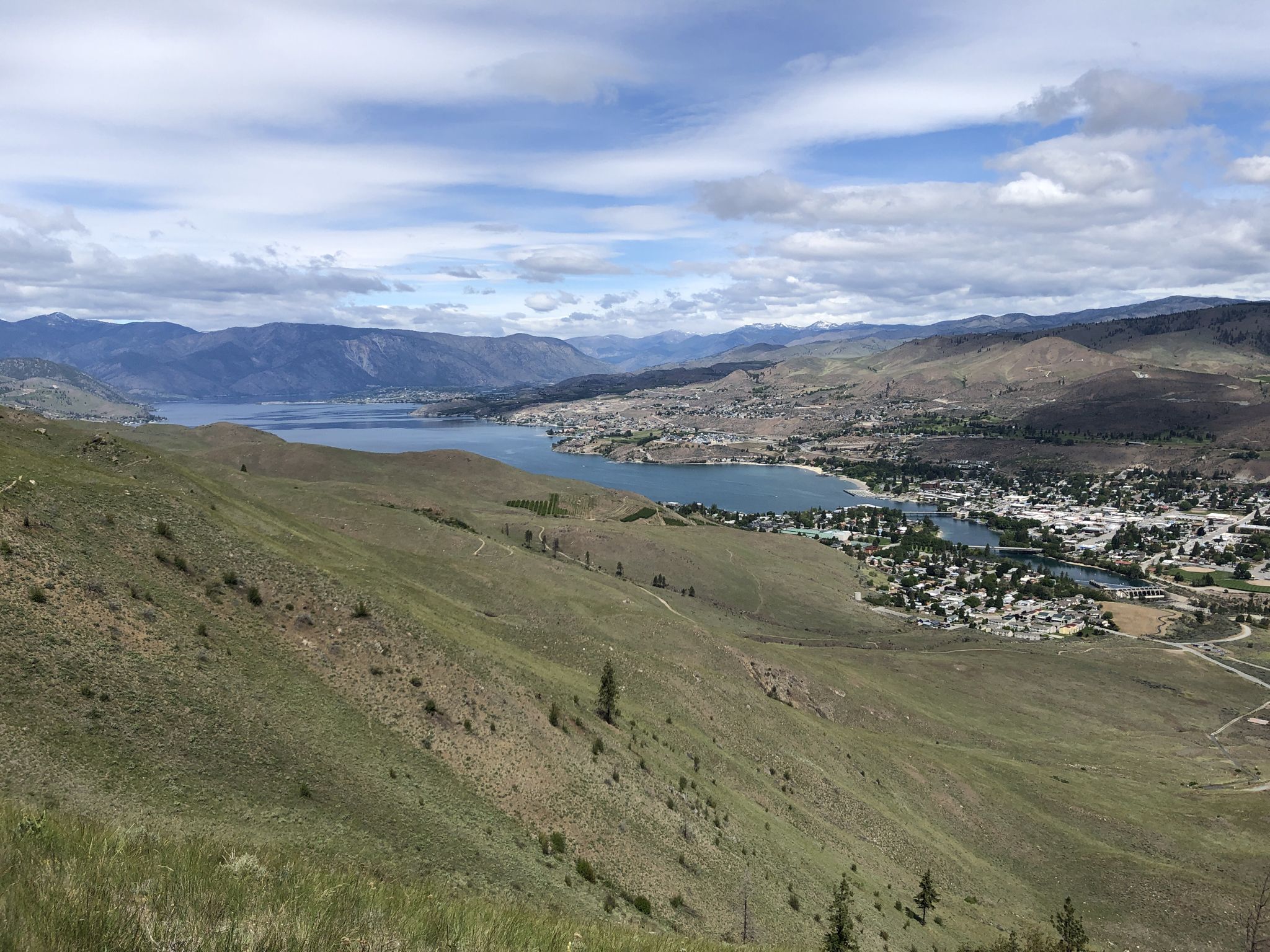 Expansive view of a lake and town nestled in a valley under a cloudy sky. - Elephant Head via Chelan Butte Trail