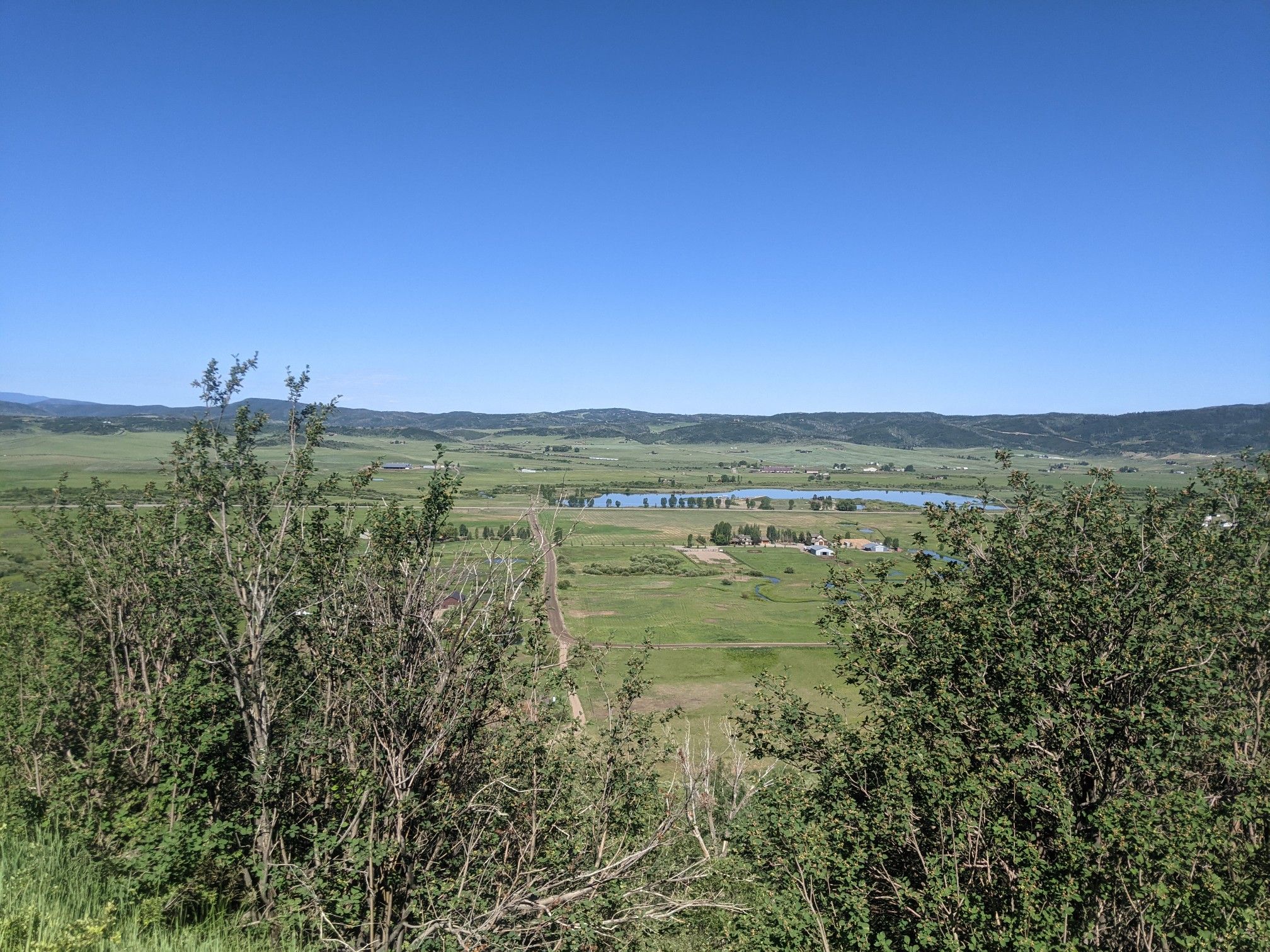 Bright sunny day over a green valley with a lake and distant mountains. - Rabbit Ears Pass
