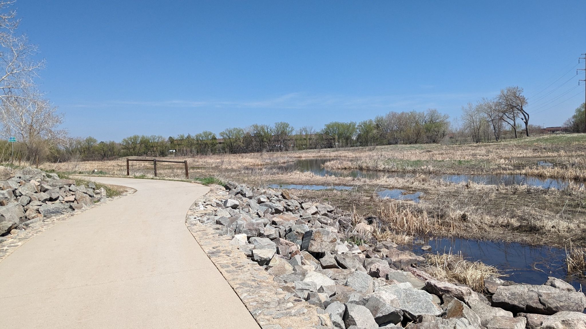 A paved path borders rocky wetlands under a bright blue sky. - Flagstaff Road Scenic Drive – Foothills Views loop from Gunbarrel
