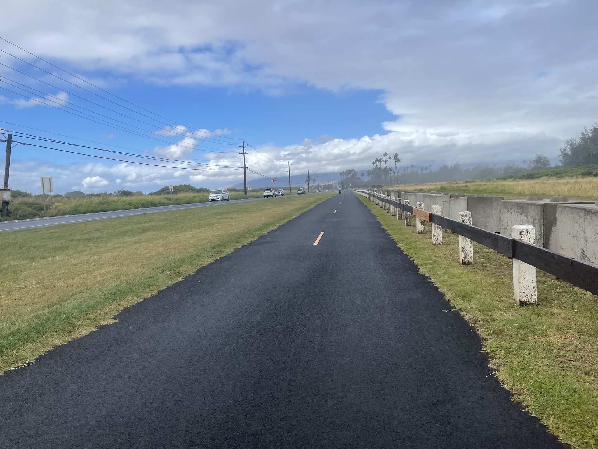 A new paved path runs alongside a road under a partly cloudy sky. - North Shore Greenway