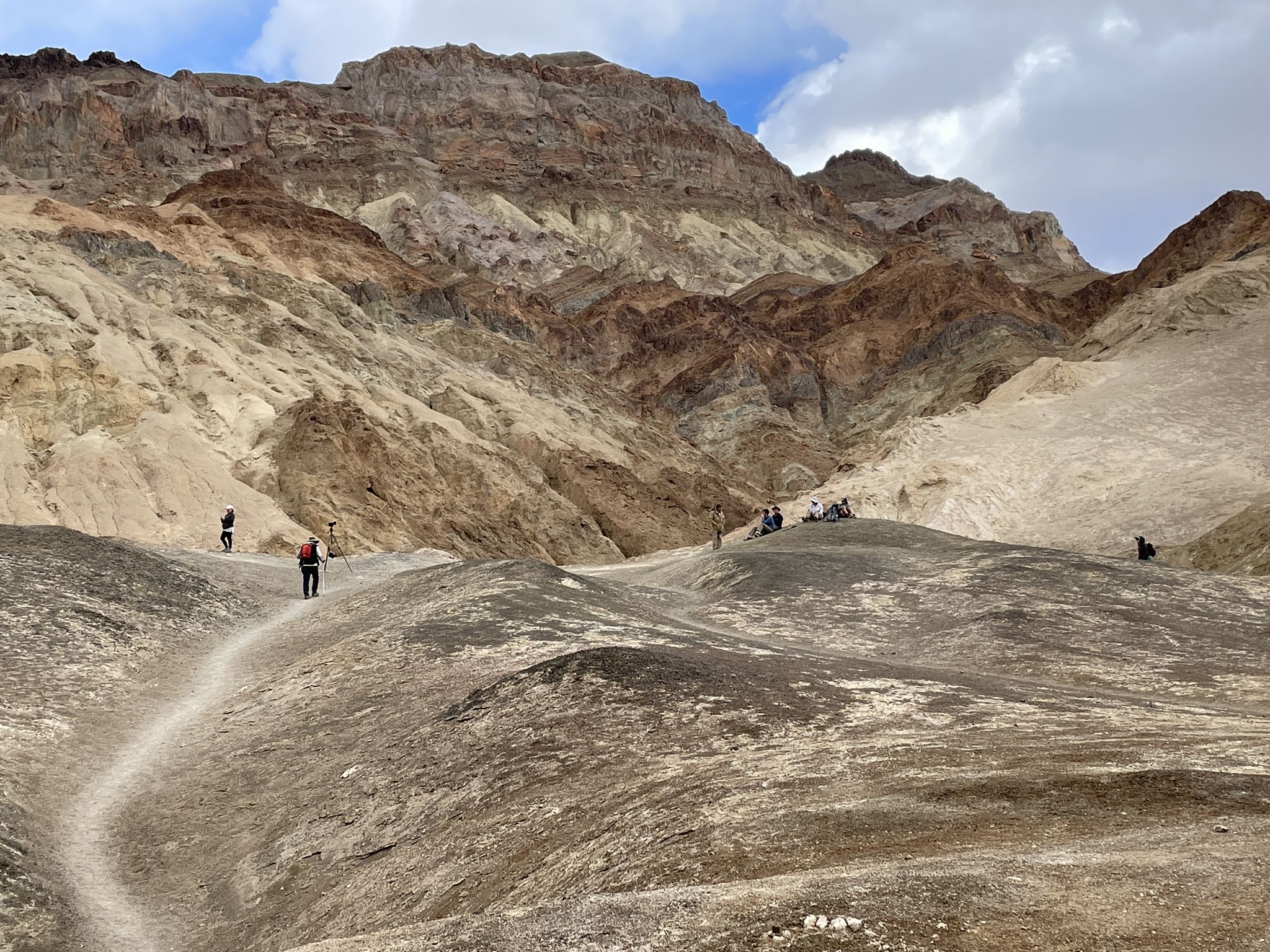 Hikers on a winding desert trail with colorful, layered mountains behind them. - Desolation Canyon Trail