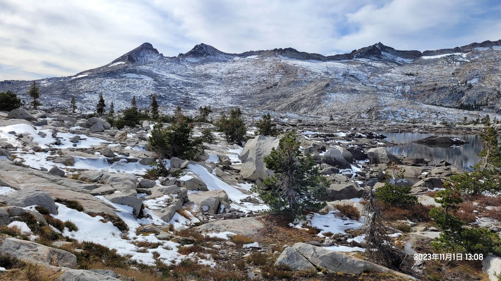 Rocky, snow-dusted landscape with small trees and a glimpse of a lake. - Lake Aloha via Pacific Crest Trail