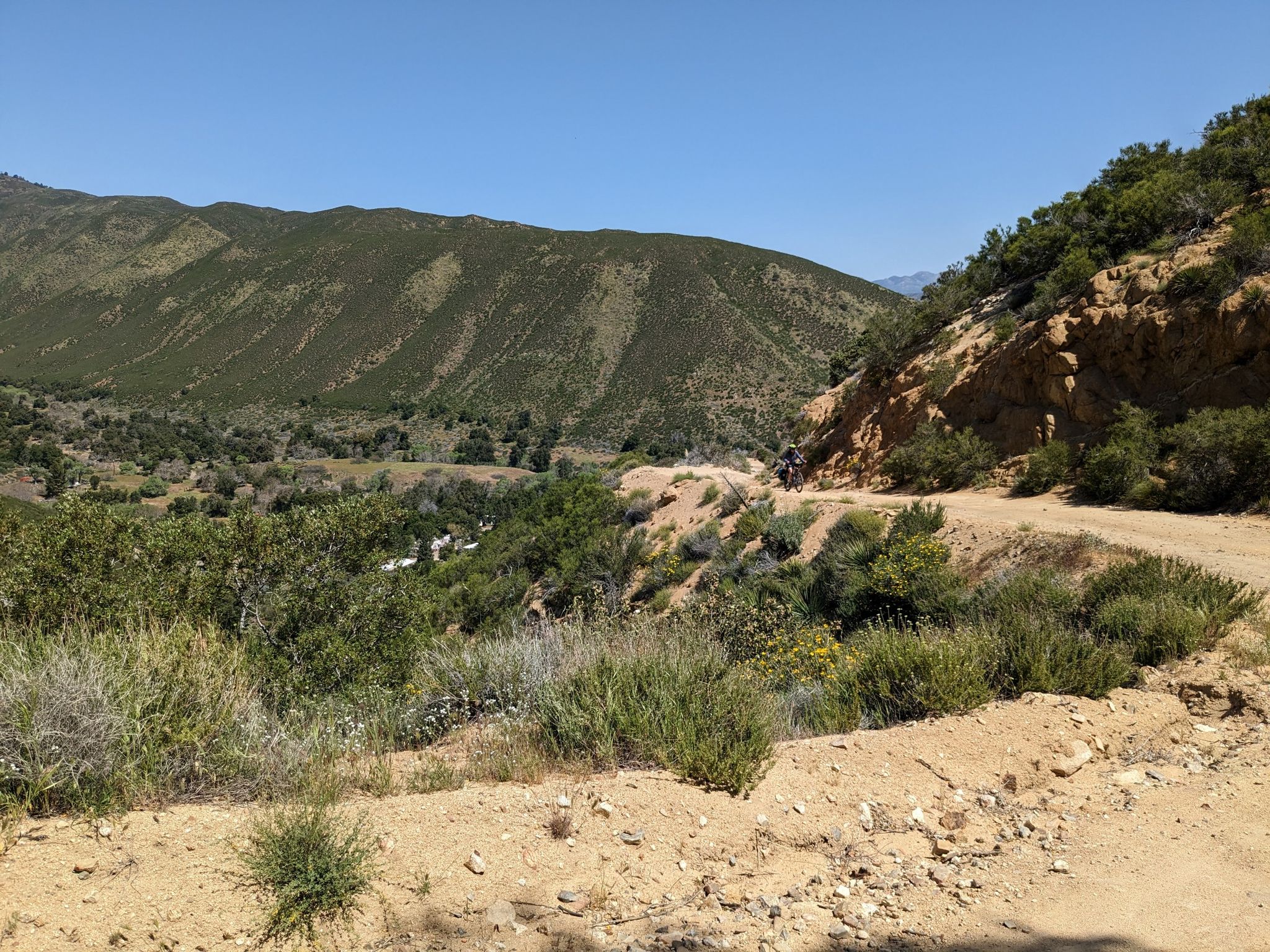 Sunny view of a dirt road overlooking a green valley and arid mountains. - Oriflamme and Chariot Canyon Trail