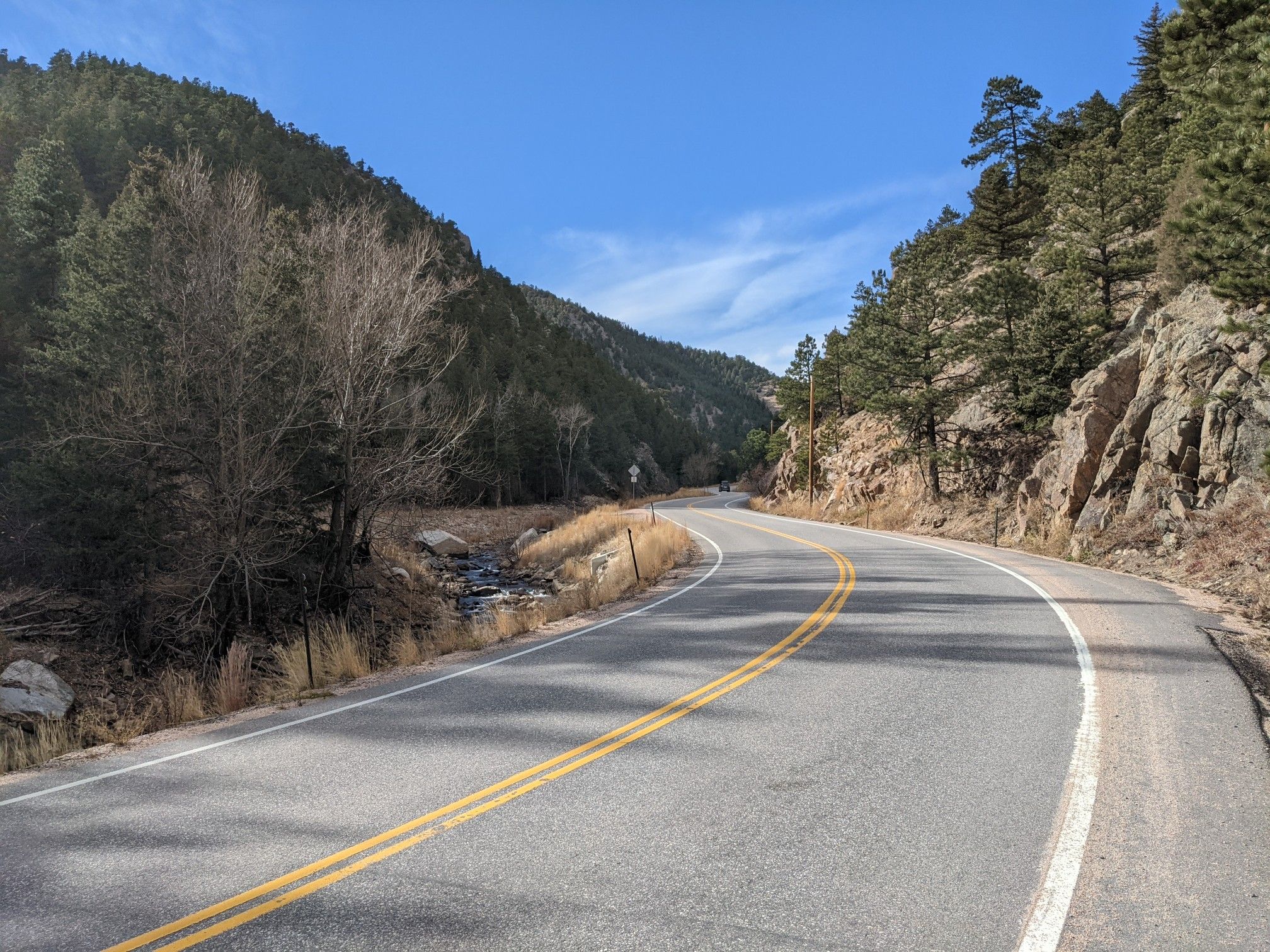 Winding road through a sunny, forested mountain valley with a stream. - Altona to Jamestown Cycling Route