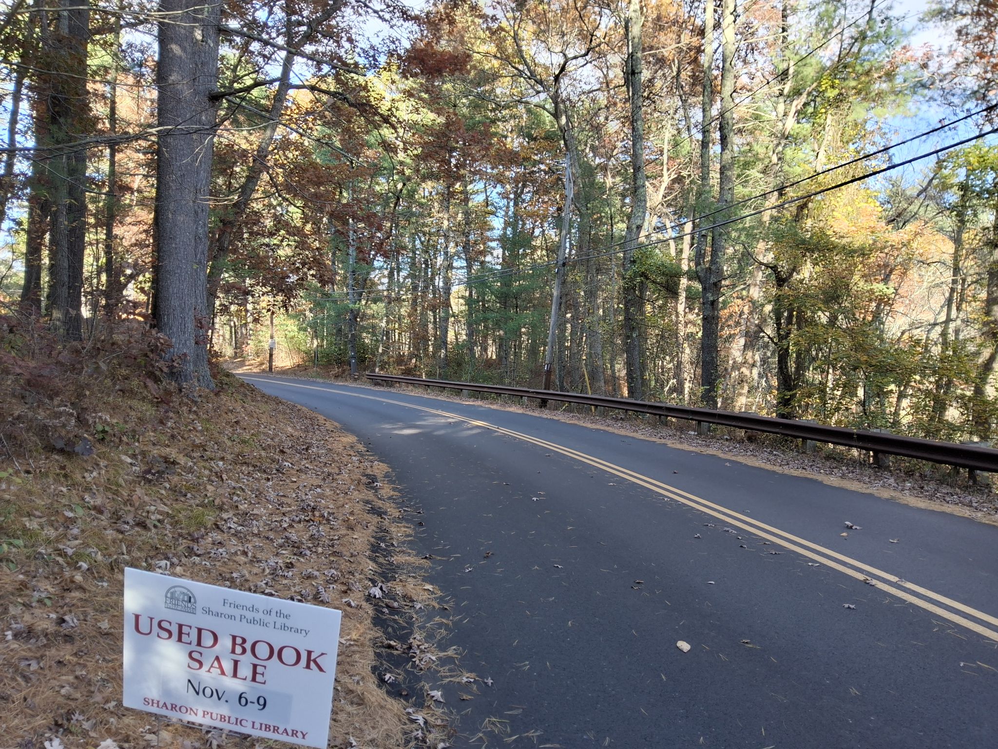 A paved road curves through a forest with a 'Used Book Sale' sign. - Moose Hill Reservation – Borderland State Park Forest loop from Borderland State Park
