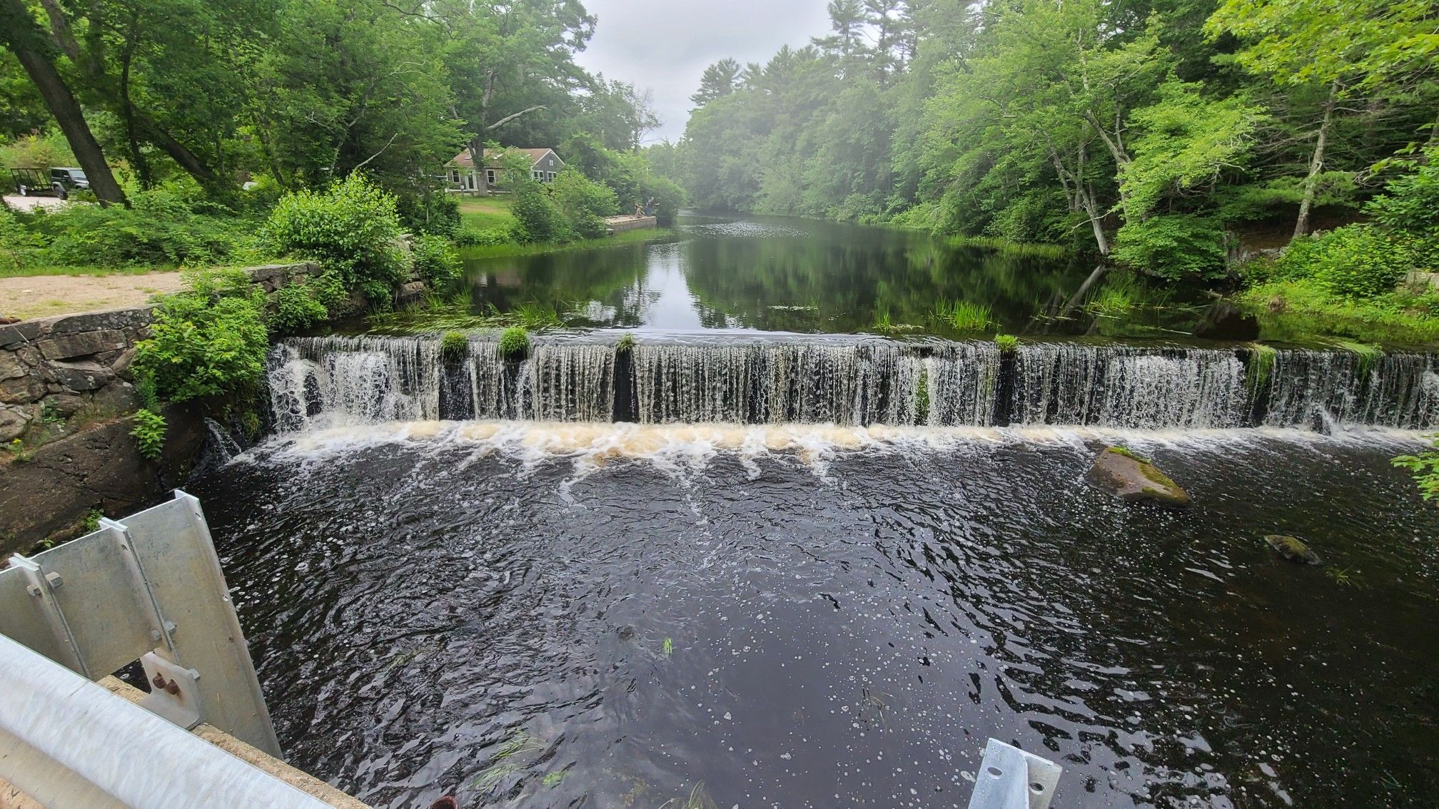A wide waterfall cascades over a dam on a river surrounded by green trees. - Arcadia Management Area – Beach Pond loop from Midway Parking