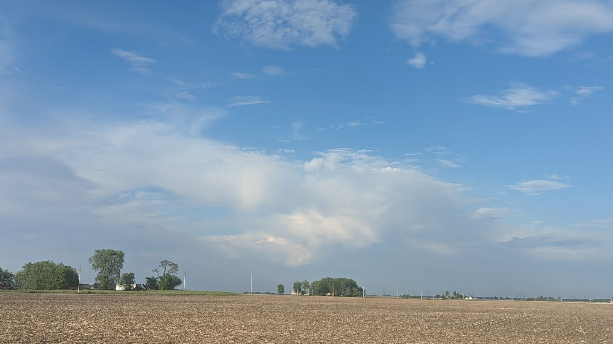 Expansive tilled field under a bright, partly cloudy blue sky with distant trees. - Urbana to Rantoul