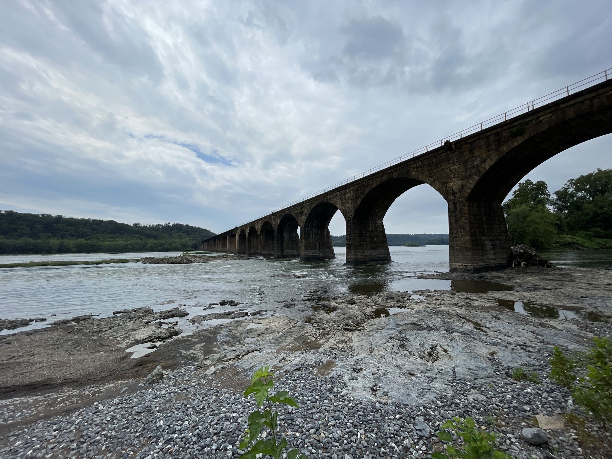 Long stone arch bridge spanning a wide river with rocky banks. - Safe Harbor Railroad Bridge loop from Marietta