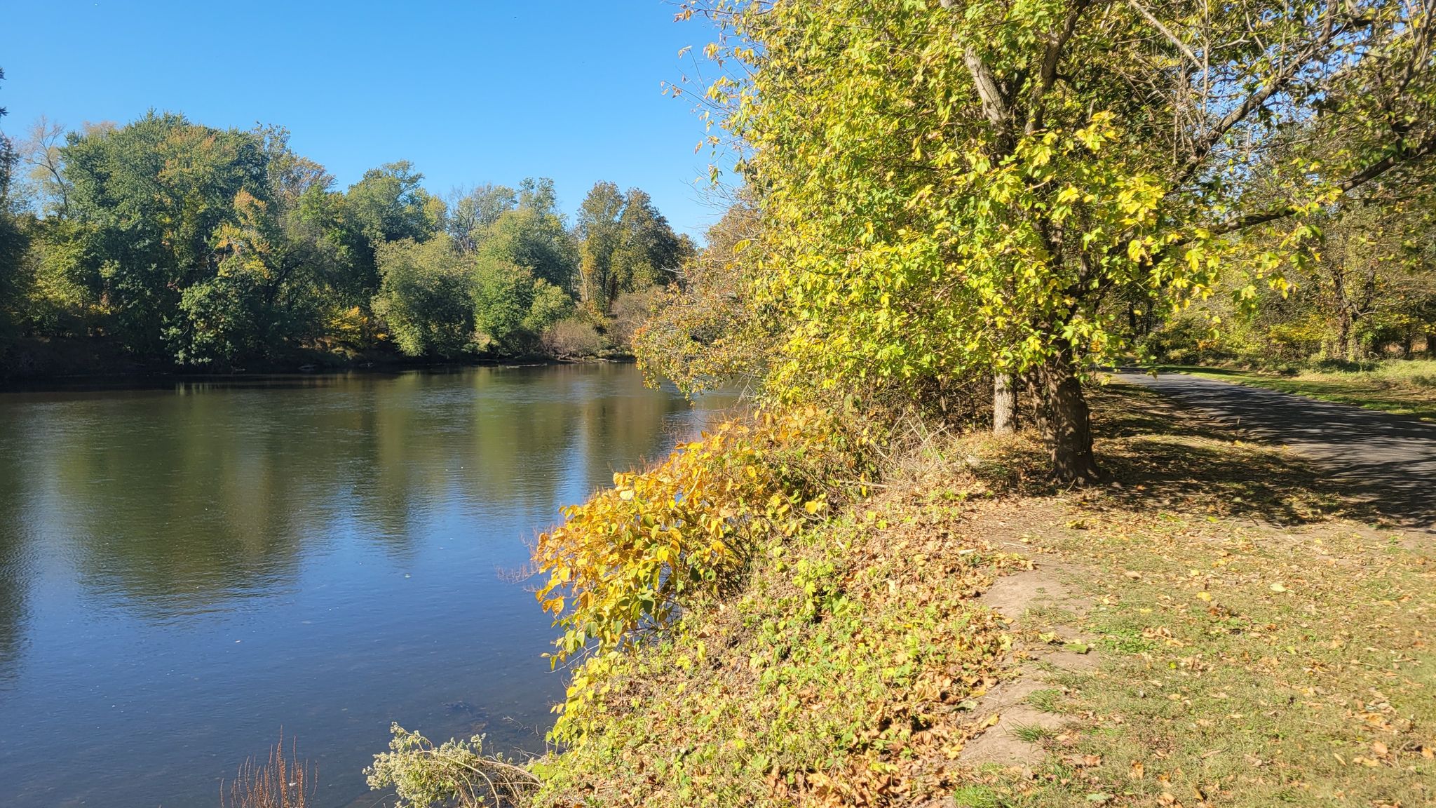 Calm river with vibrant autumn trees and a sunny path alongside. - View from Sullivan's Bridge – National Memorial Arch loop from Devon