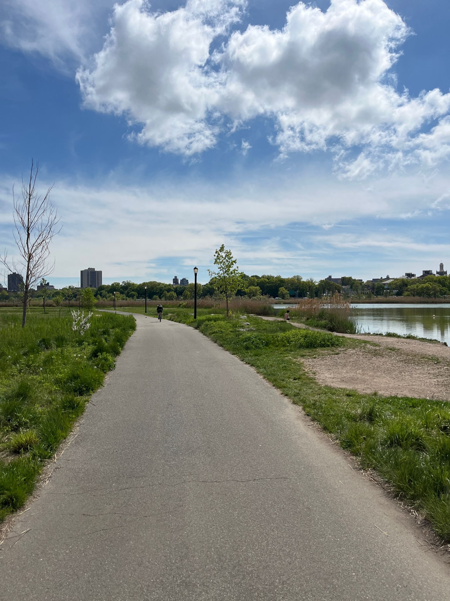 Paved path through a green park beside a lake under a bright, cloudy sky. - Flushing Meadow Park and Meadow Lake