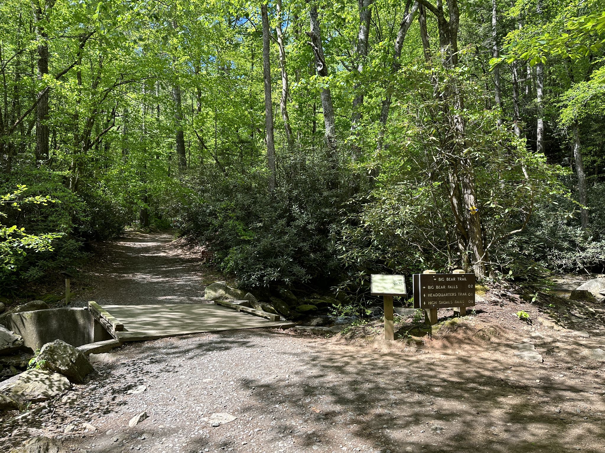 A shaded forest trail features a small bridge and wooden informational signs. - Shinny Creek Loop Trail