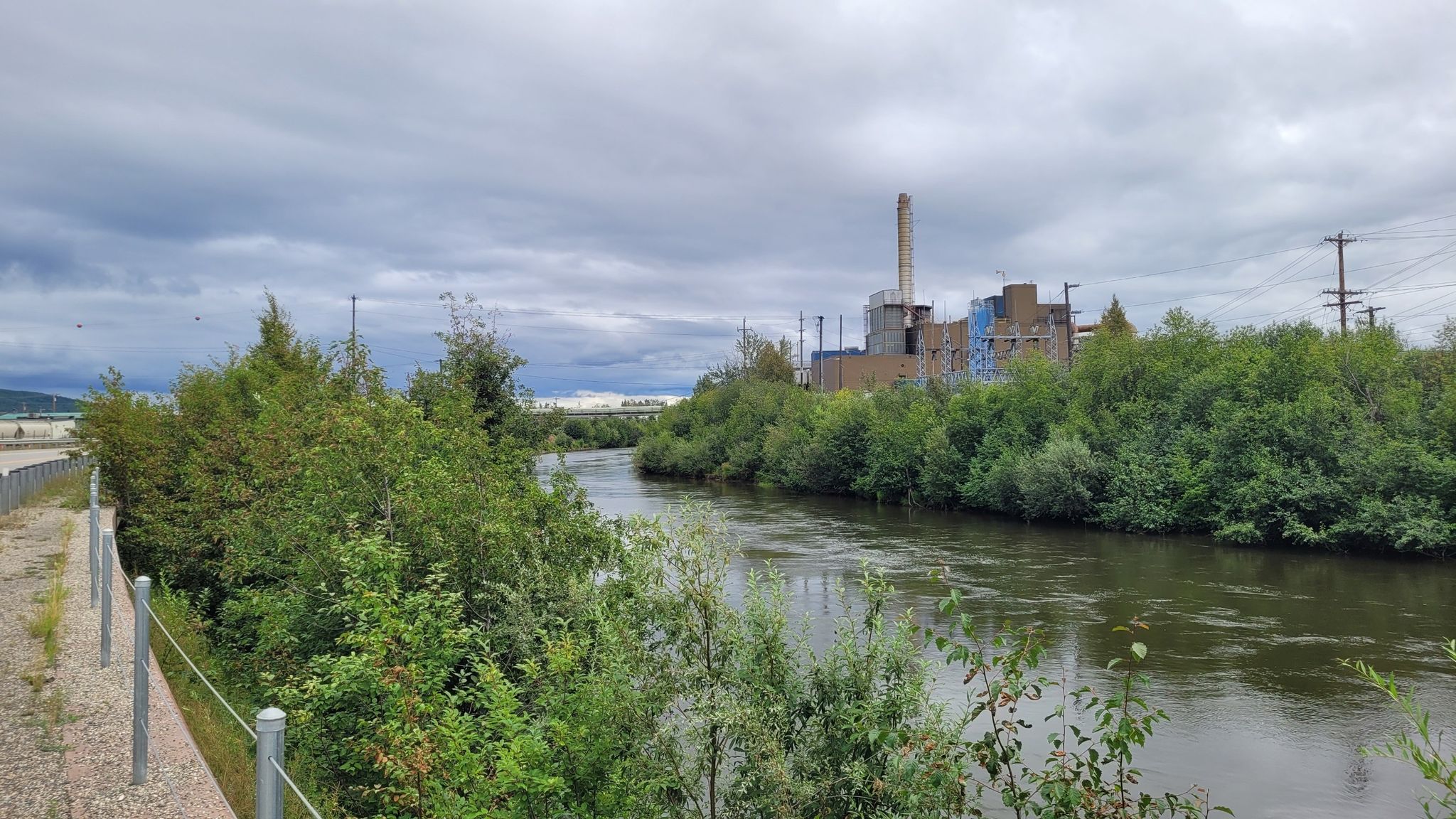 A wide river flows past an industrial building under a cloudy sky. - Sheep Creek  to Goldstream Road loop