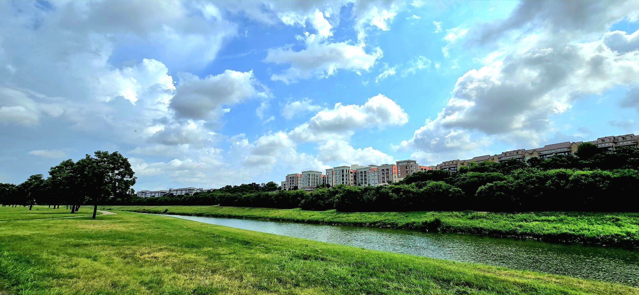 A wide river flows through green fields under a partly cloudy sky. - Trinity Park Loop