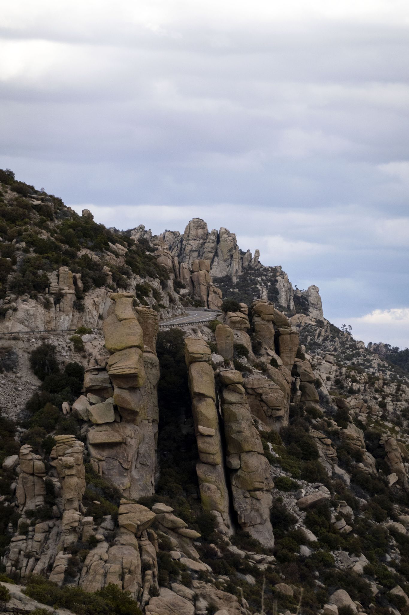 Dramatic stacked rock formations on a steep mountain slope under a cloudy sky. - View from East Ski Run Road – Mount Lemmon climb summit loop from Soldier Camp