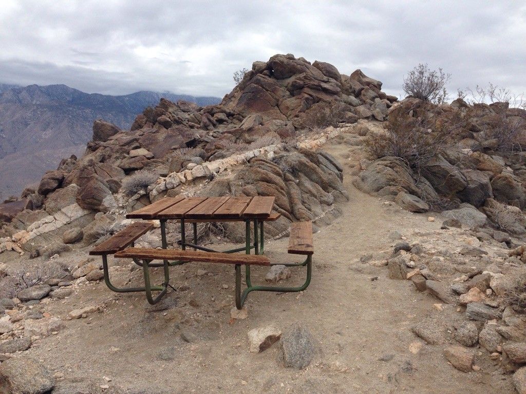 A wooden picnic table on a rocky mountain path under an overcast sky. - Murray Hill Loop – San Bernardino National Forest