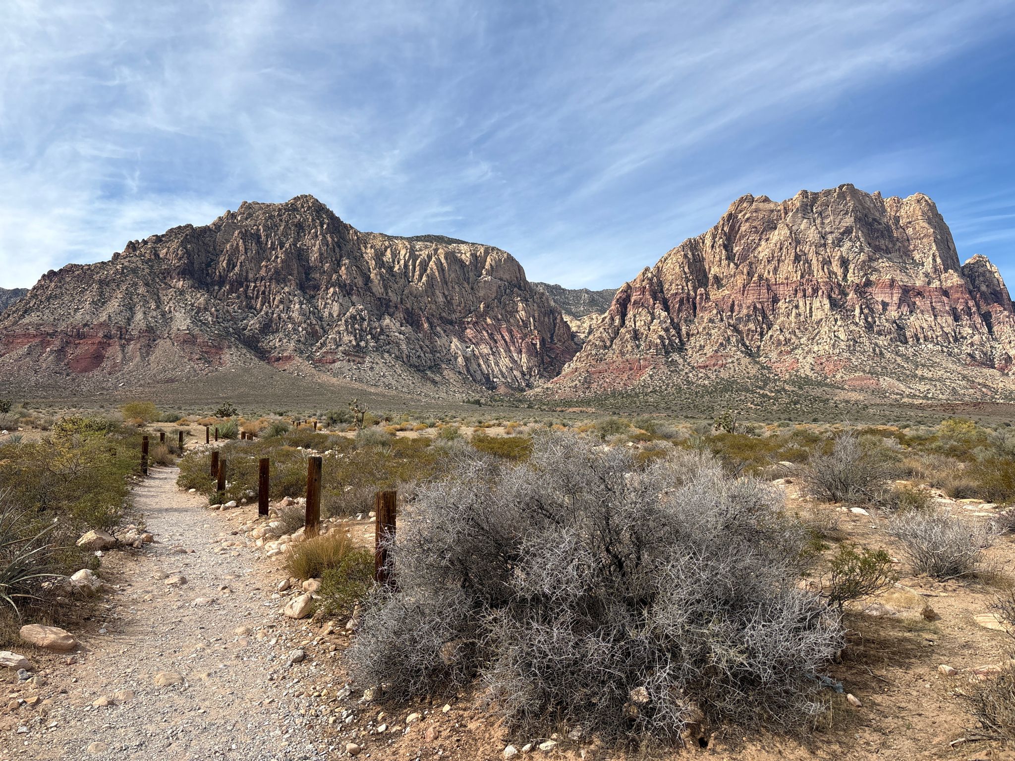 Desert trail with wooden posts leading towards distant red rock mountains. - First Creek Canyon Trail