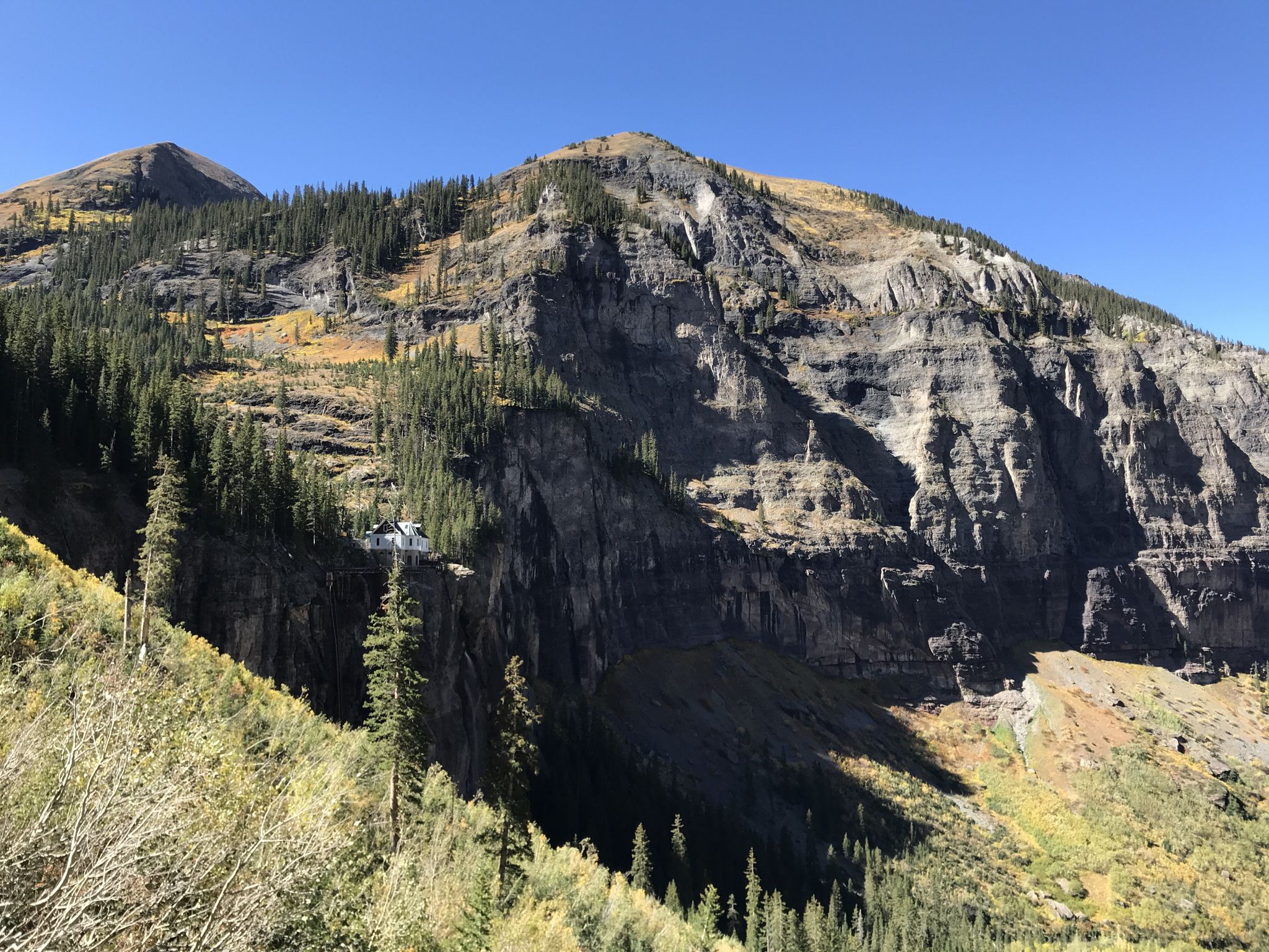 Massive, rugged mountain face covered in trees and rock formations, sunny. - Ajax Peak – Valley View loop from Bridal Veil Falls