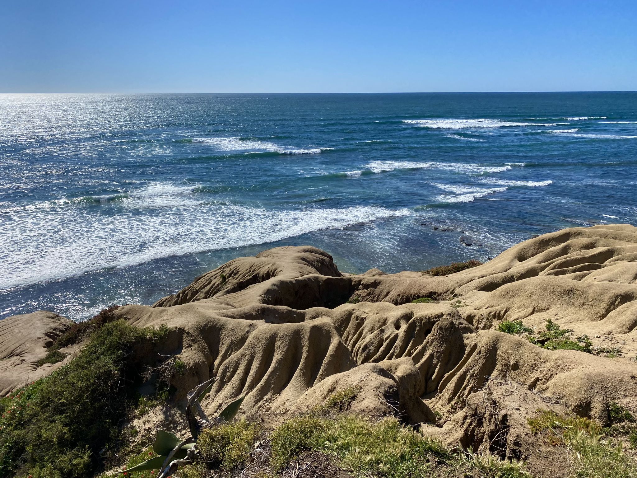 Rugged, eroded sandstone cliffs meet the blue ocean with white waves. - Sunset Cliffs Natural Park – Sunset Cliffs Sea Caves loop from Point Loma