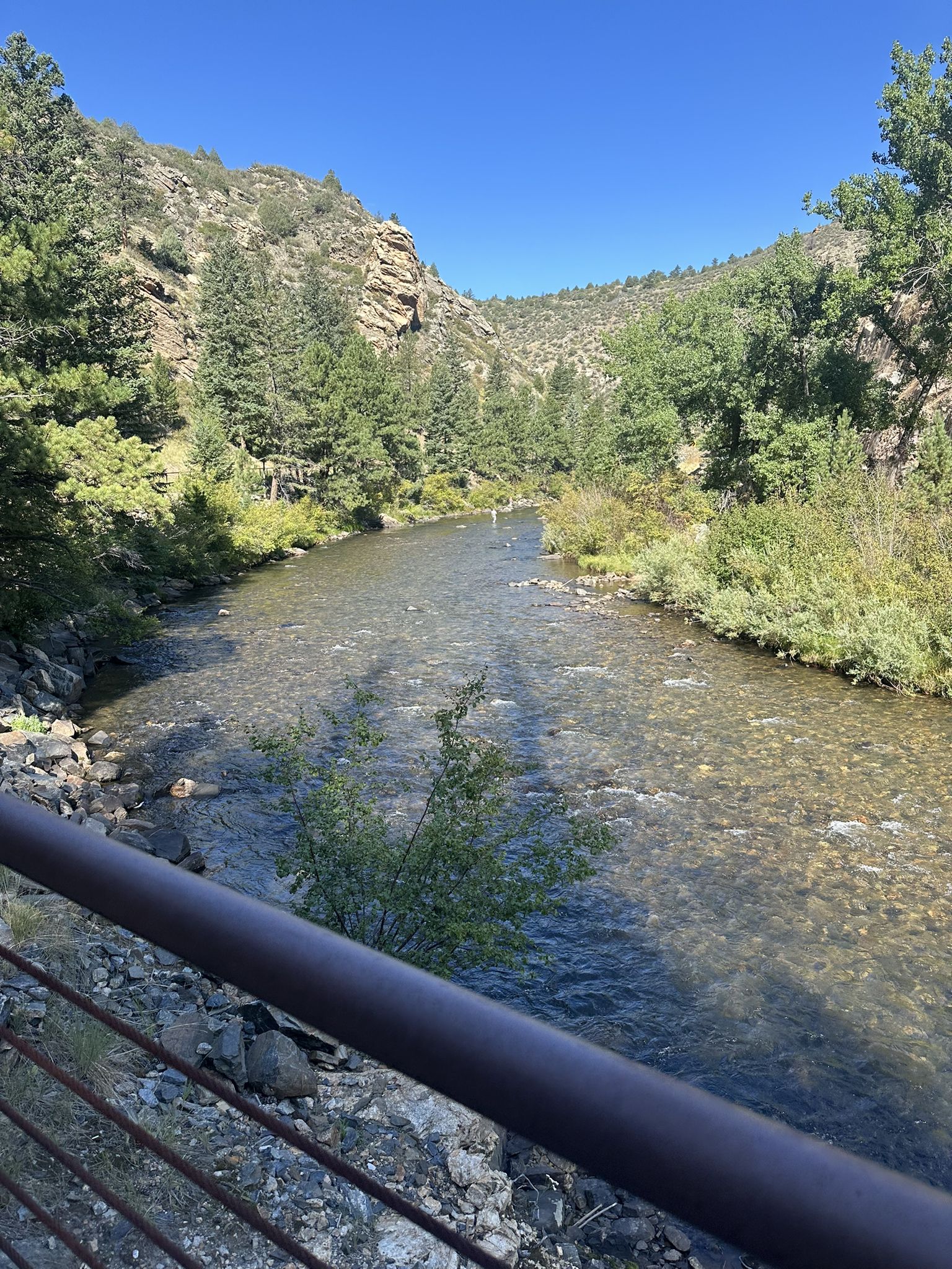 Clear river flowing through a sunny, rocky valley with forested hillsides. - Peaks to Plains Trail