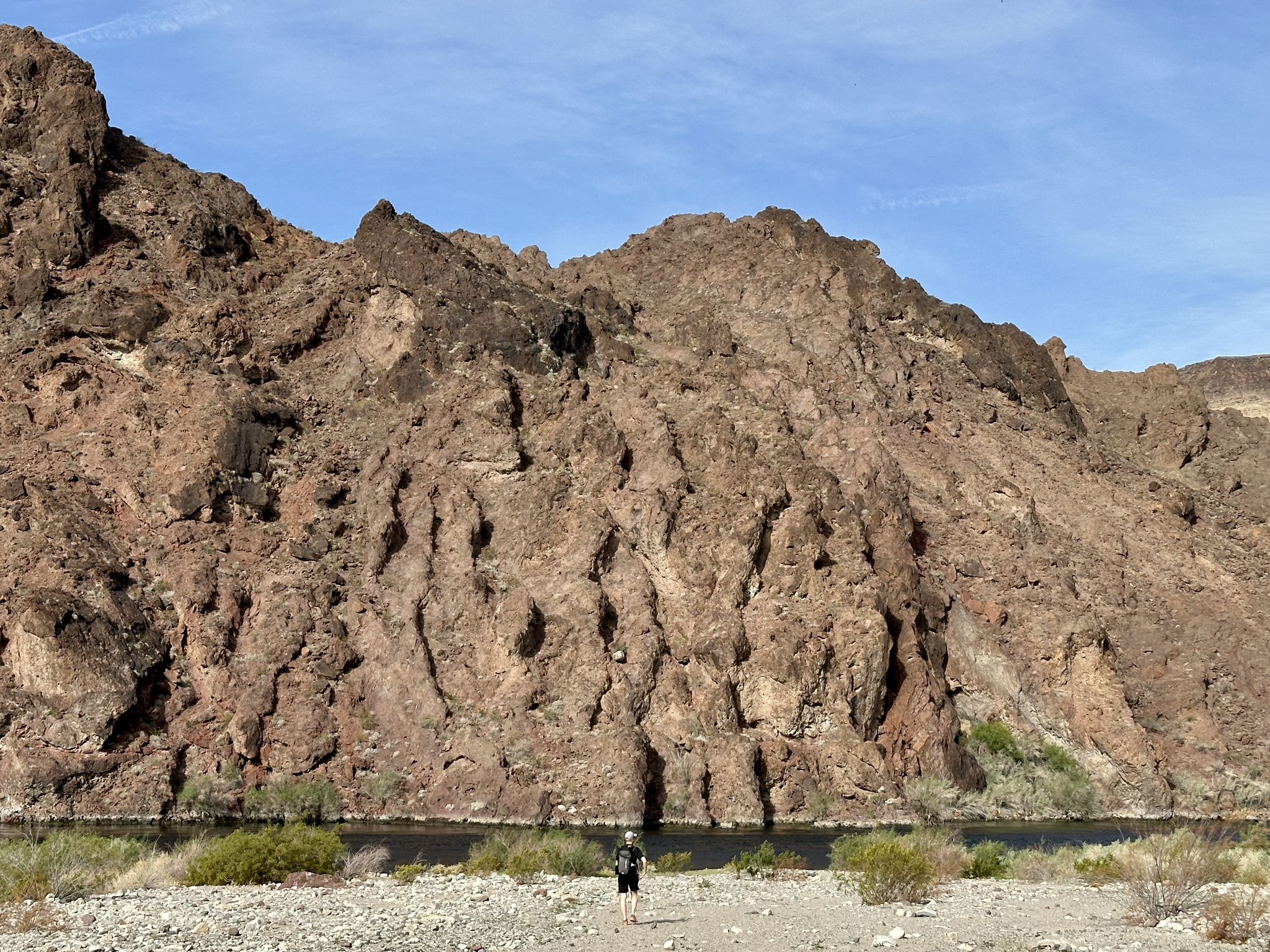 Person standing by a river at the base of large rocky mountains under a clear sky. - White Rock Canyon Trail