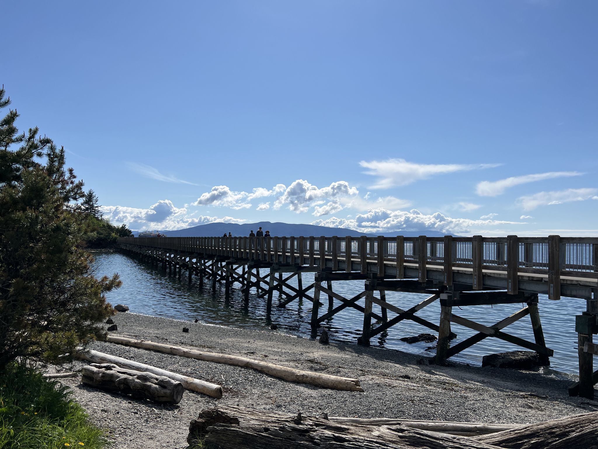 Long wooden pier over rocky beach and water, with distant mountains and clouds. - Arroyo Nature Reserve loop via US Bike Route 97