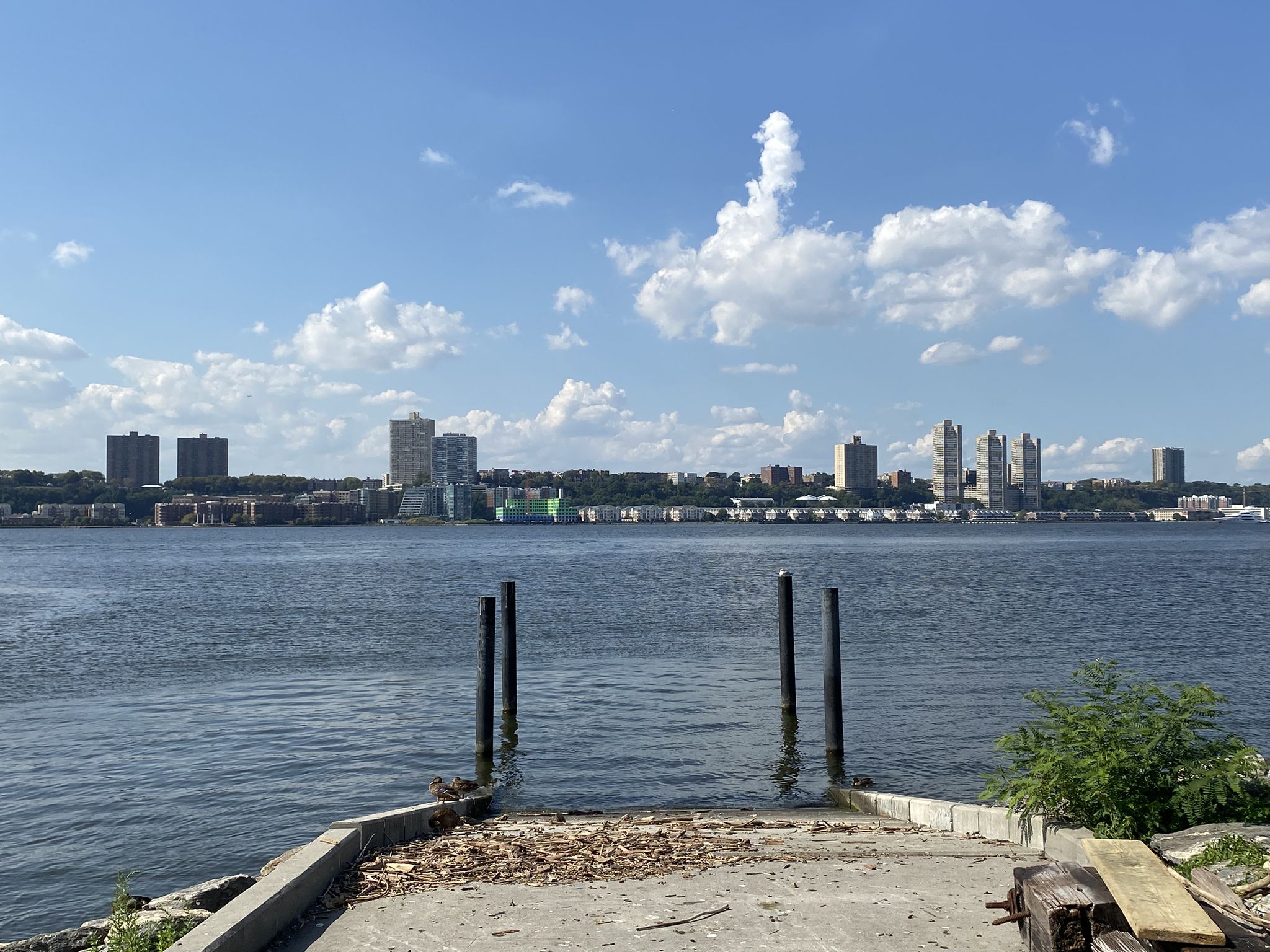 Waterfront view with distant city skyline and blue sky with white clouds. - Hudson River Greenway