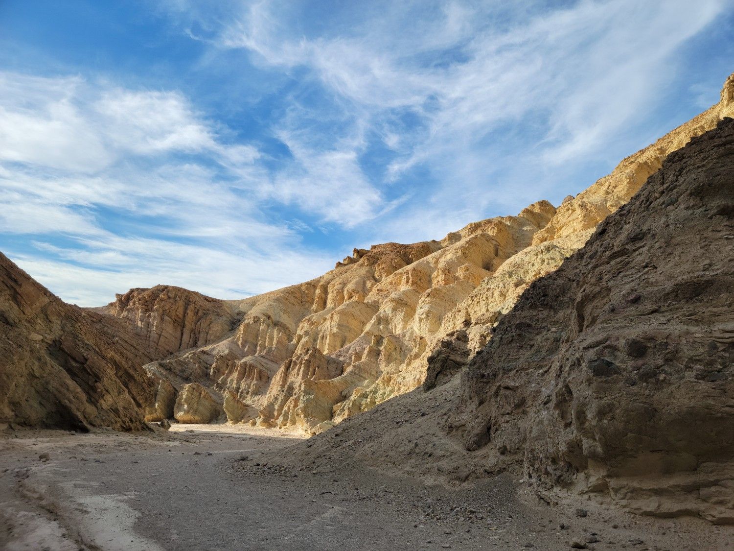 Sandy wash winding through a canyon with sunlit rock formations and blue sky. - Golden Canyon Trail