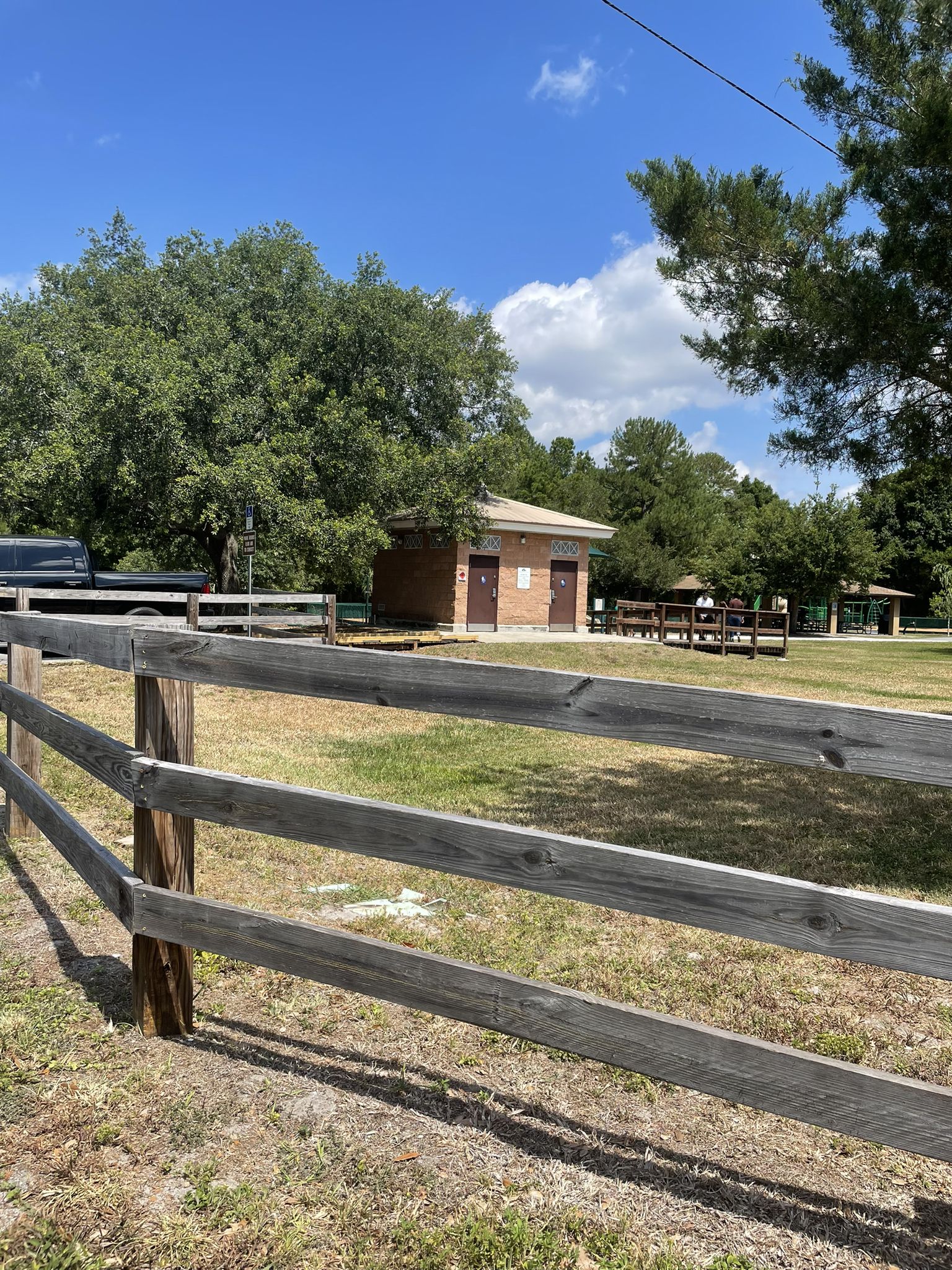 A park restroom building behind a wooden fence, with picnic tables nearby. - Lake Osceola – Howell Creek Fishing Pavilion loop from Winter Park