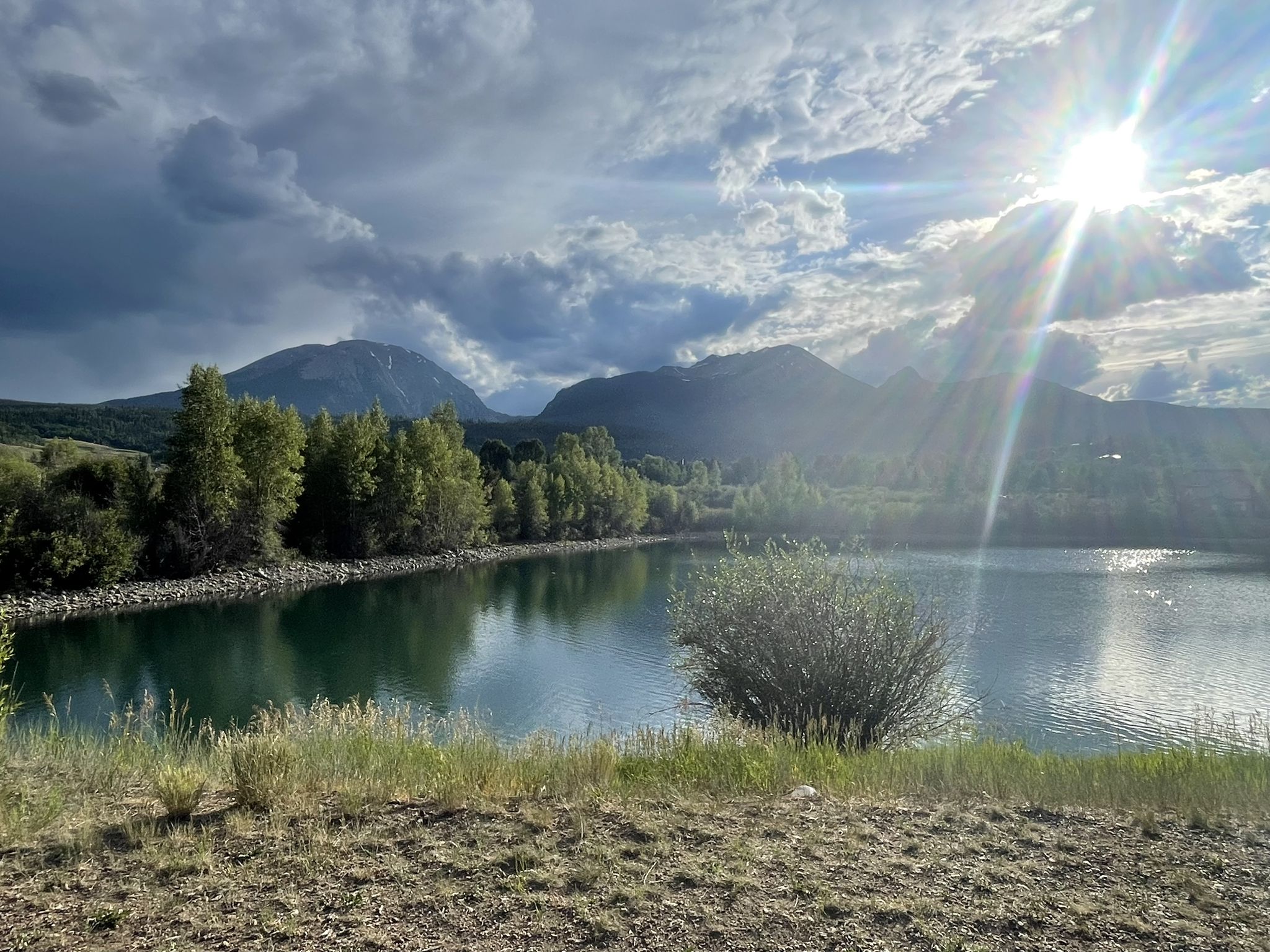 Sunburst over a calm lake with mountains and dramatic clouds. - North Pond Park loop from Willowbrook