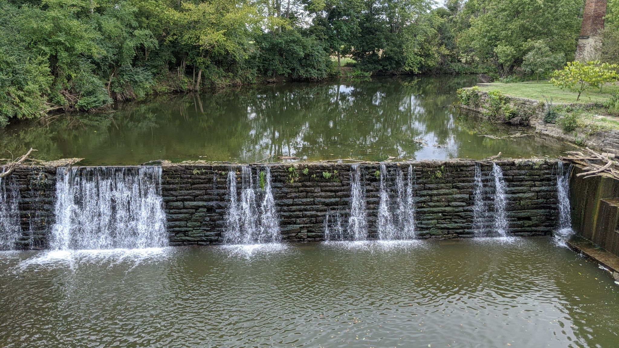 Water cascades over a stone dam in a river surrounded by green trees. - Bluegrass Bike Tour: Lexington to Georgetown Loop